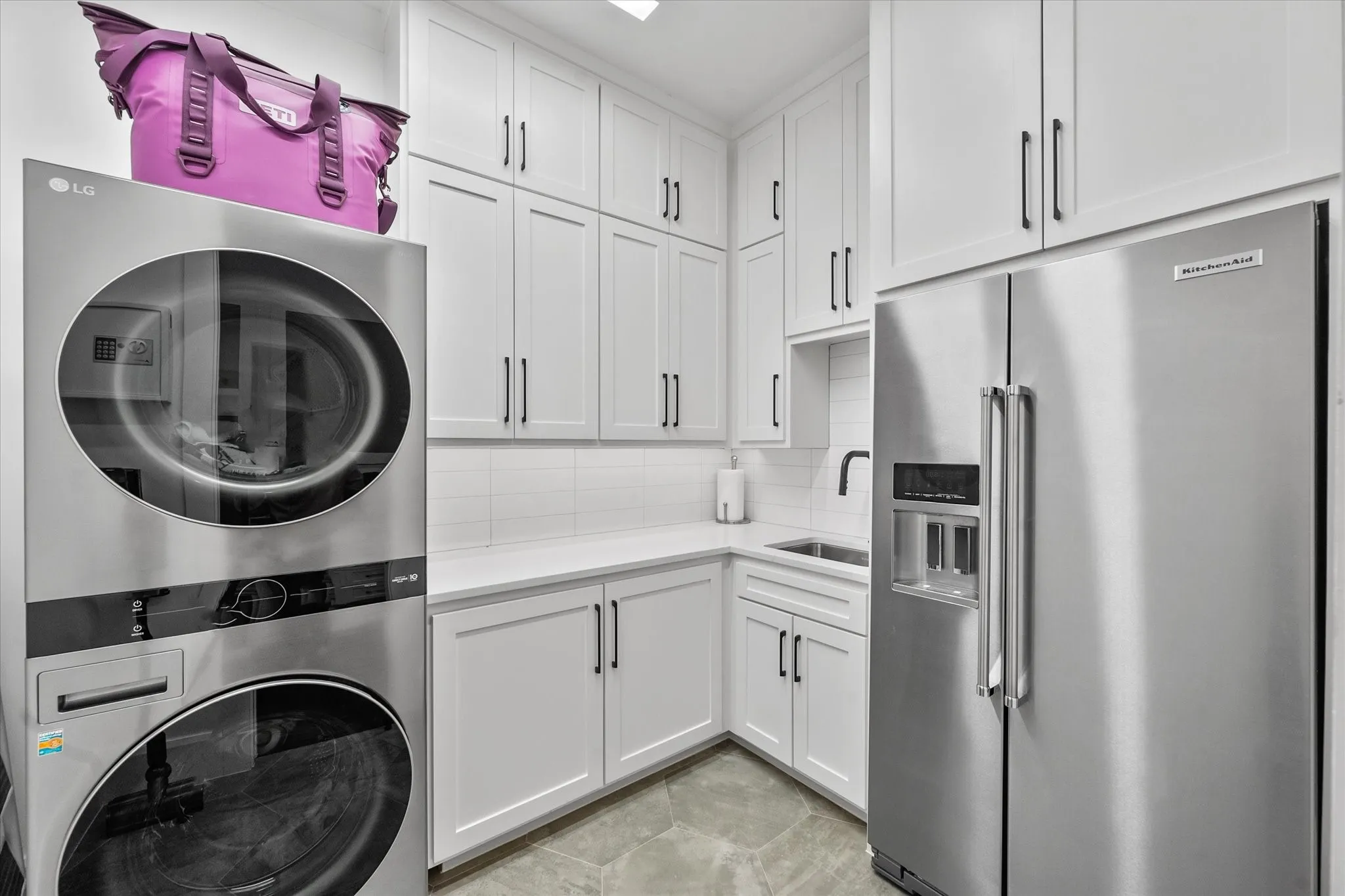 Integrated utility room featuring white shaker-style cabinetry, quartz countertops, a white subway tile backsplash, and stone-finish flooring