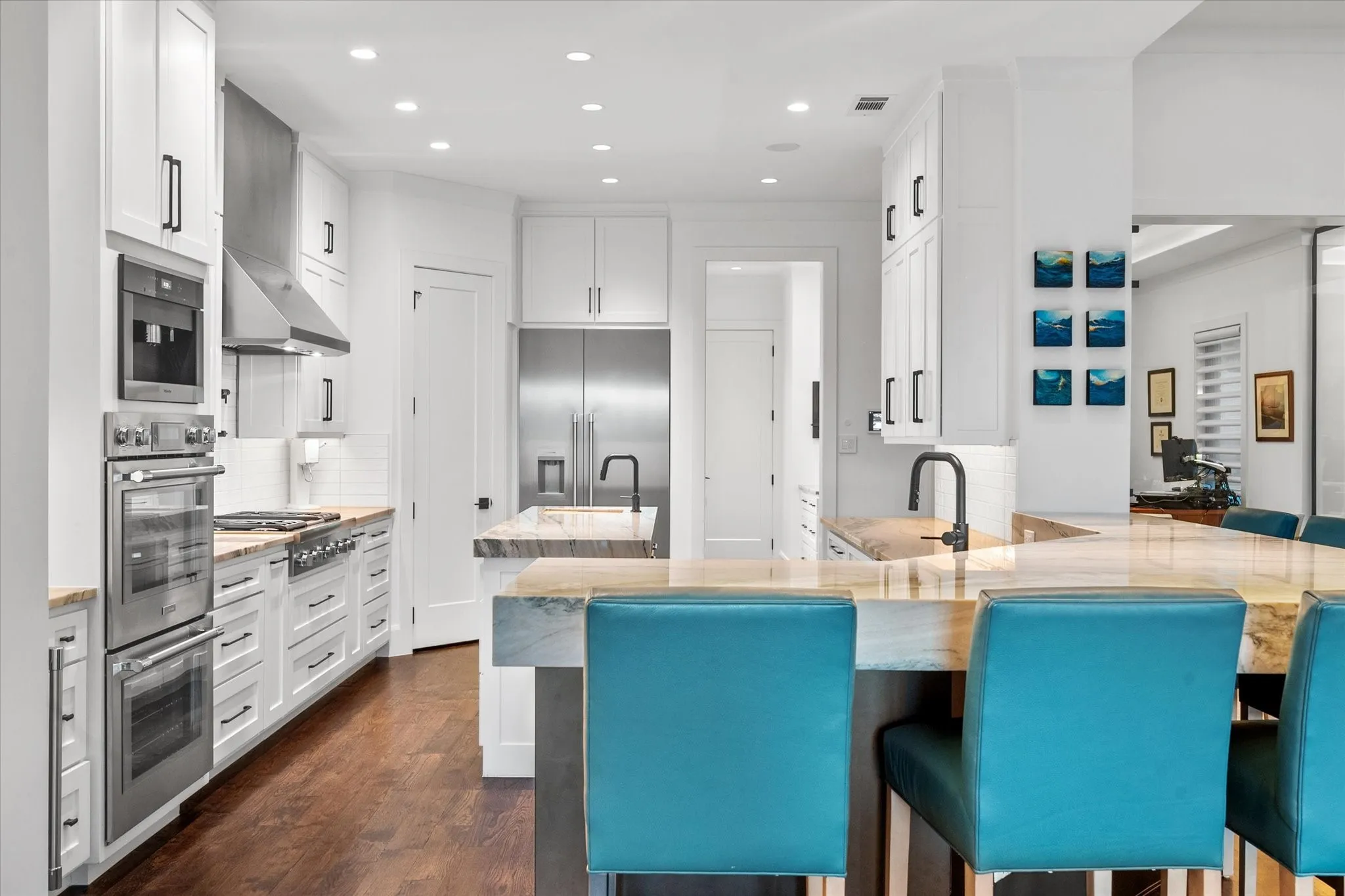 Gourmet kitchen with extensive white cabinetry, stainless steel appliances including a built-in double oven and large refrigerator, a stone countertop island with seating, and wood-finish flooring