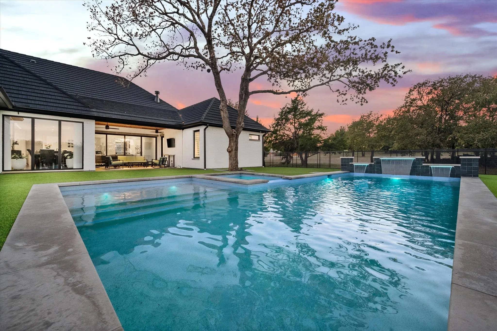 Spacious backyard oasis featuring a rectangular swimming pool with integrated spa and cascading water features