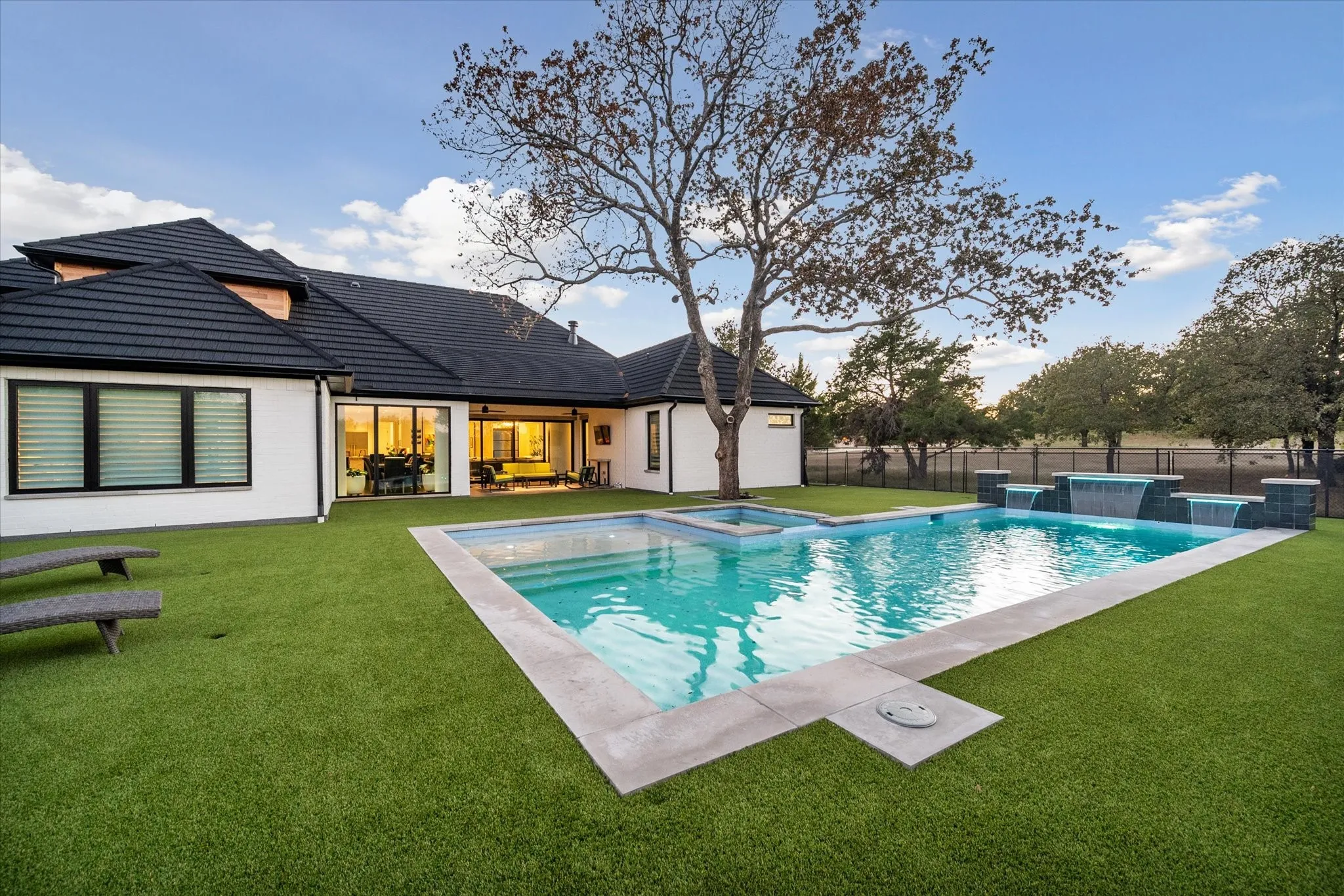 Rear exterior featuring a rectangular pool with integrated spa, multiple water features, and a surrounding artificial turf lawn
