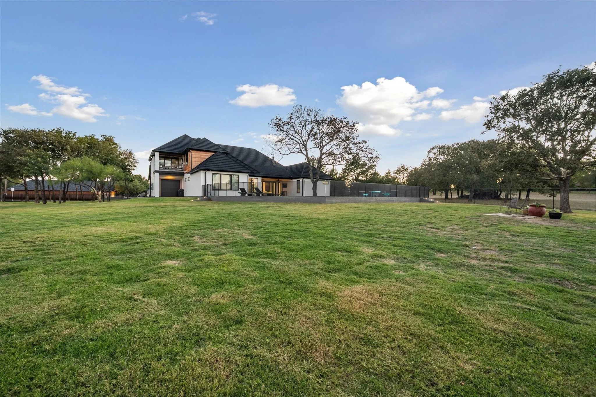 Expansive green lawn bordering a modern two-story residence with a black roof and white and wood-finish exterior