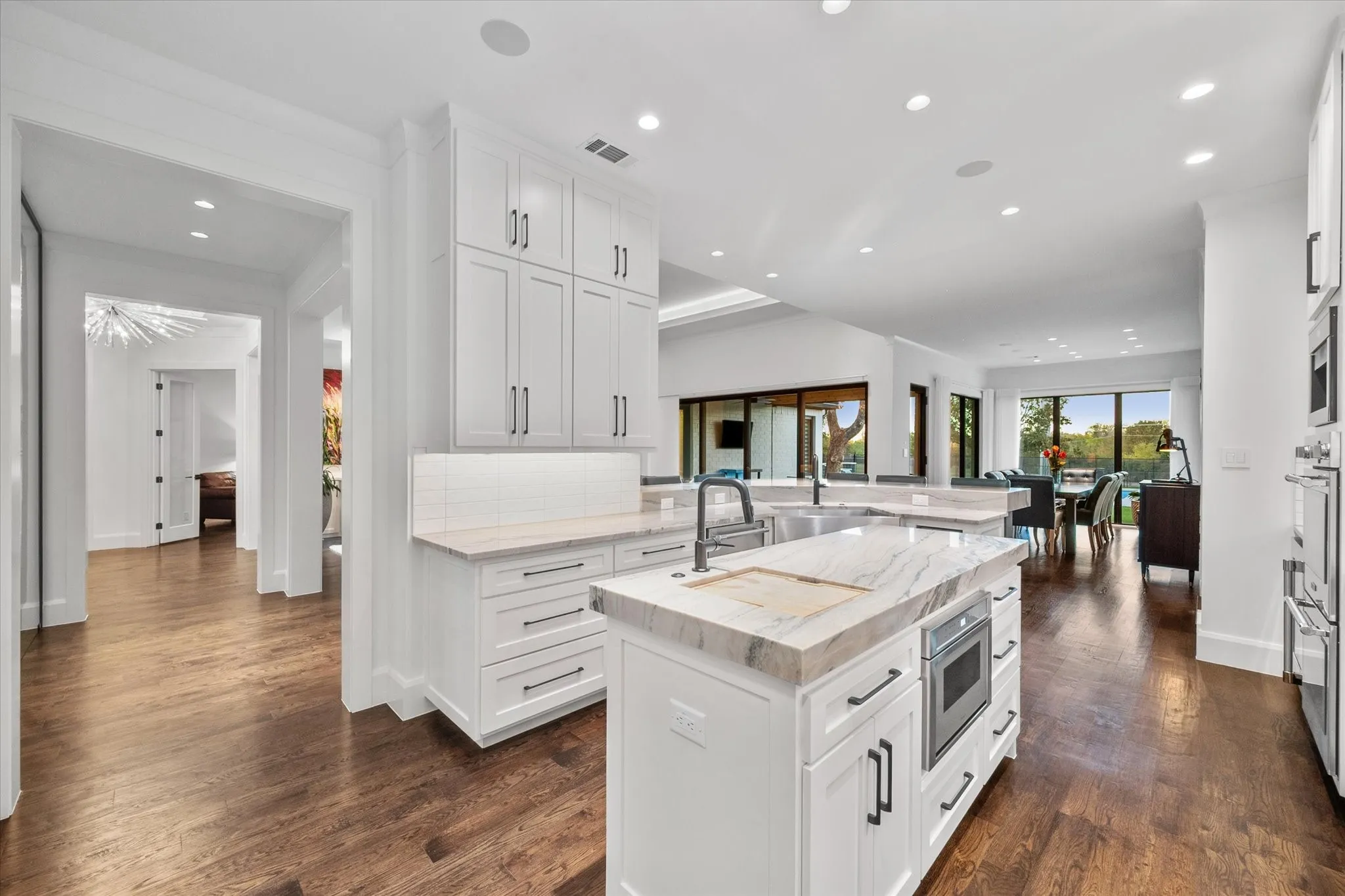 Gourmet kitchen featuring a central island with integrated microwave, dual sinks, white shaker cabinetry with dark hardware, and light-toned countertops