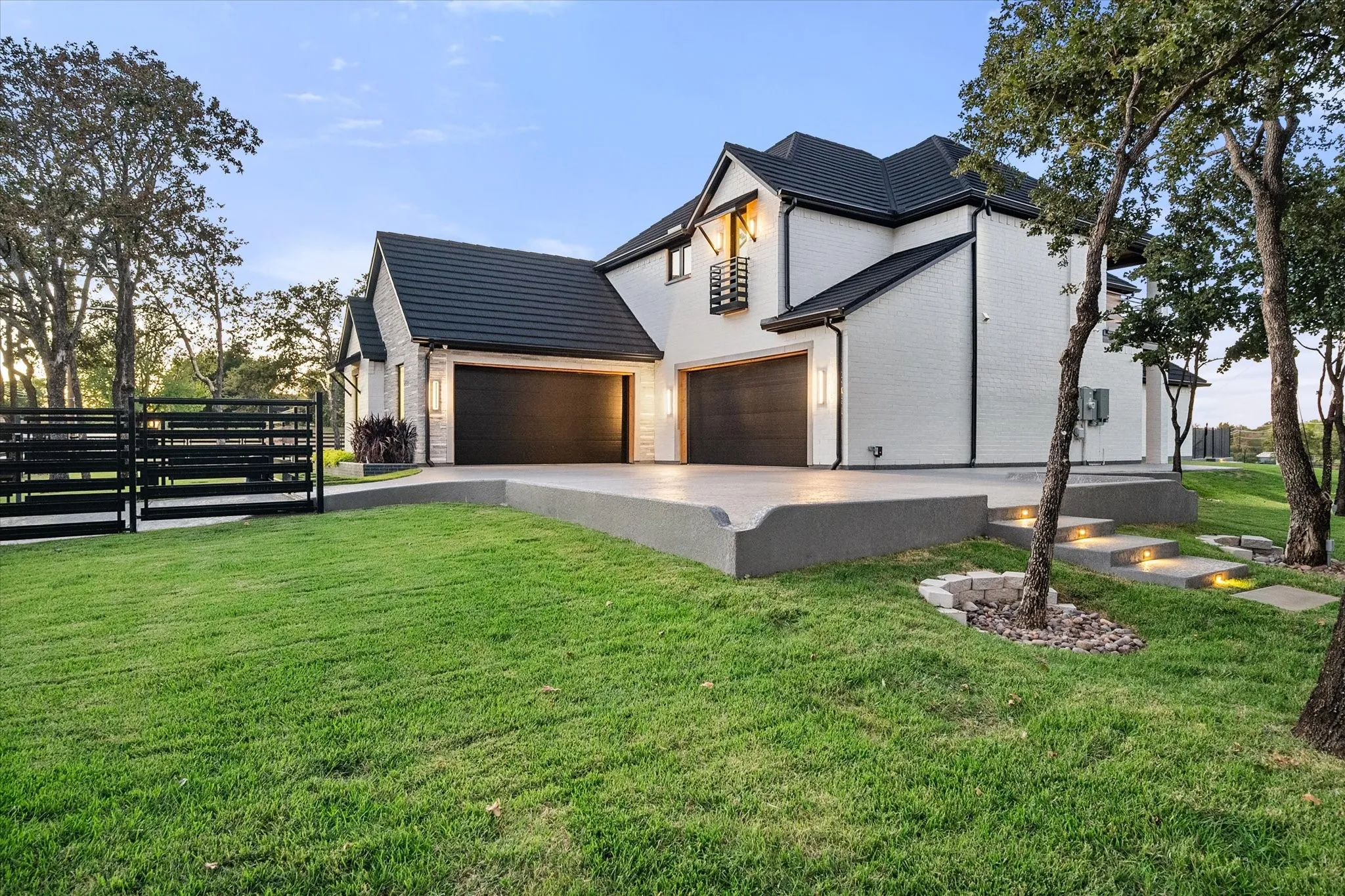 Contemporary residence featuring a white brick exterior, black roof, and dual garage doors