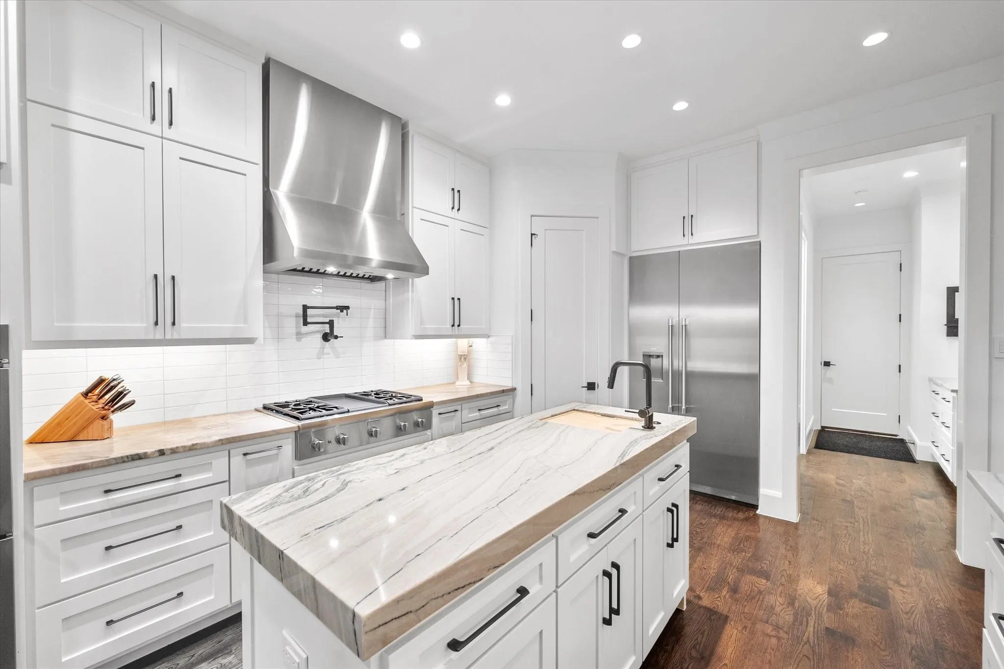 Kitchen featuring a central island with a unique veined countertop, white shaker cabinetry, stainless steel appliances, a pot filler, and wood-finish flooring