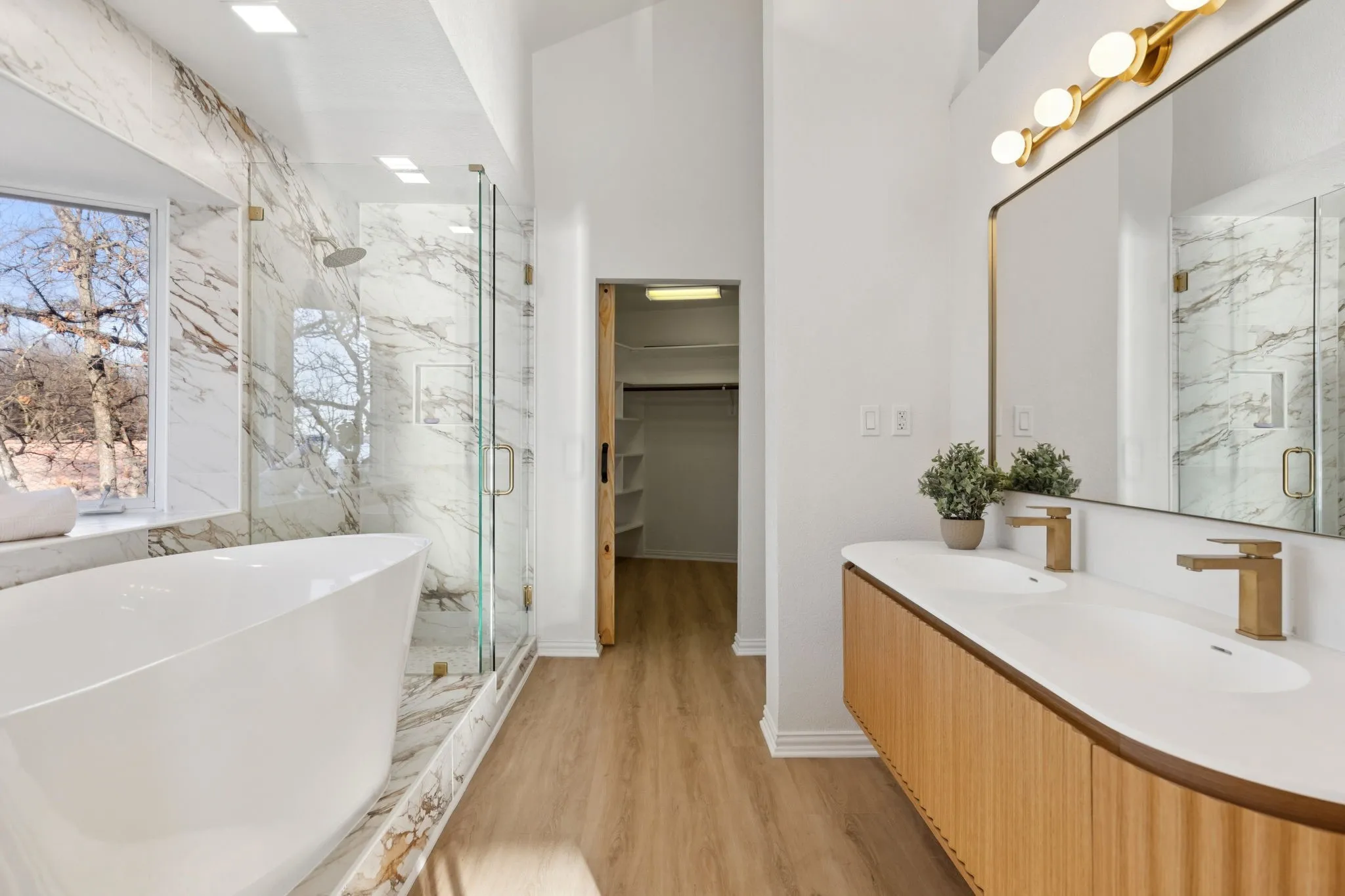 Bathroom featuring a marble finish shower, double vanity, a freestanding tub, a spacious closet, and light wood-type flooring