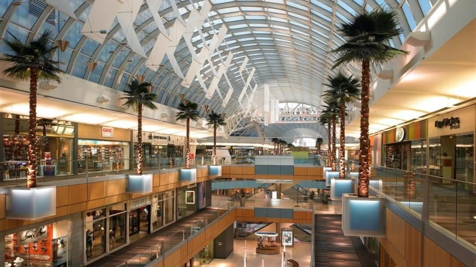 Multi-level retail interior featuring a vaulted glass ceiling and integrated palm trees