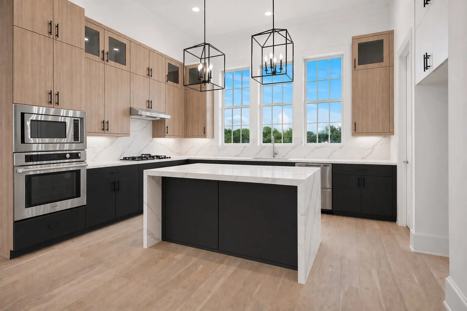 Contemporary kitchen featuring a waterfall island with a stone countertop, light wood-finish flooring, stainless steel appliances, and dual black geometric pendant lights