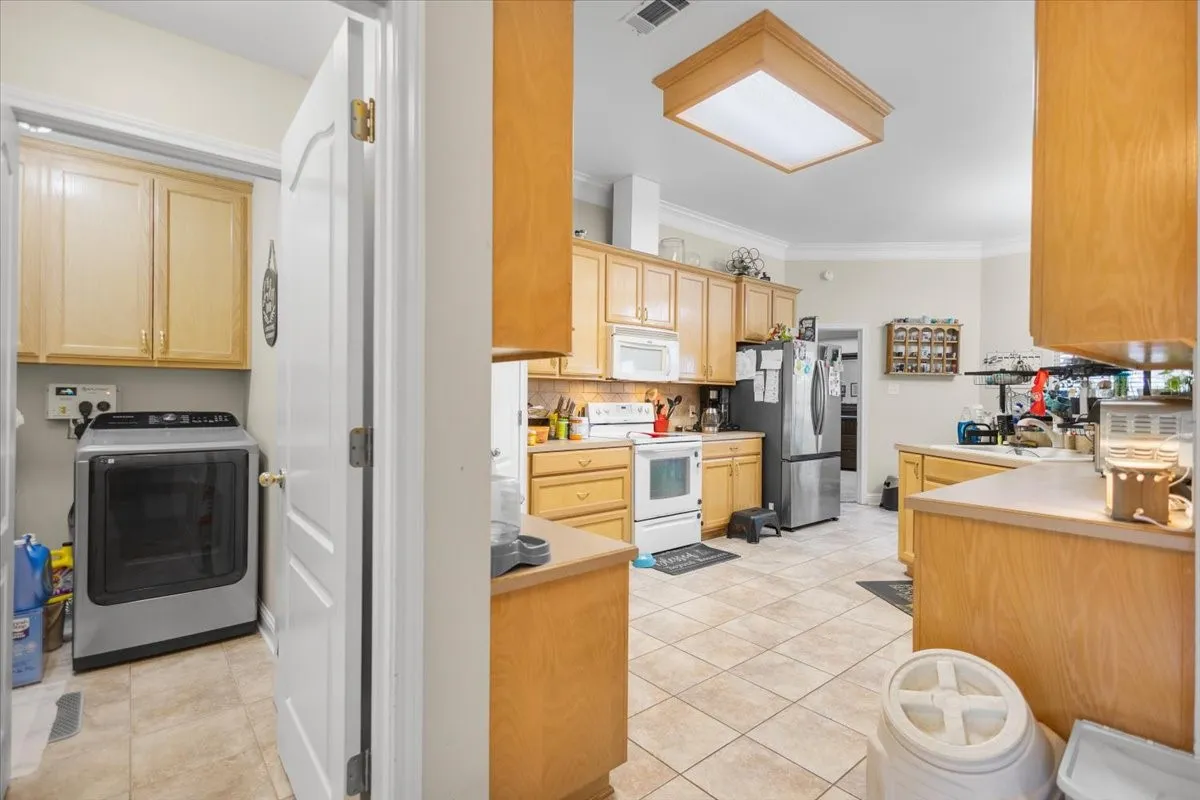Tiled kitchen flooring with light wood-finish cabinetry, a stainless steel refrigerator, and ample countertop space