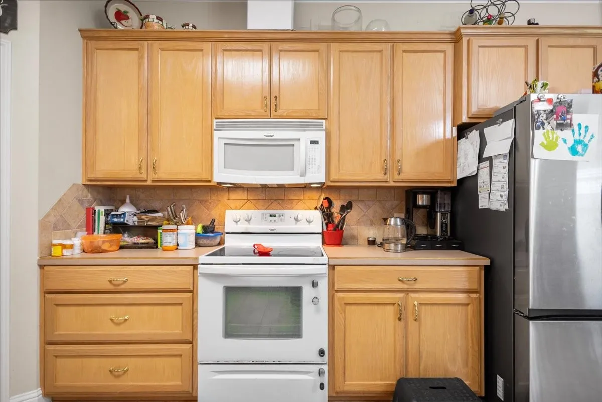 Kitchen featuring light wood-finish cabinetry, a built-in microwave, an electric range, and a tile backsplash