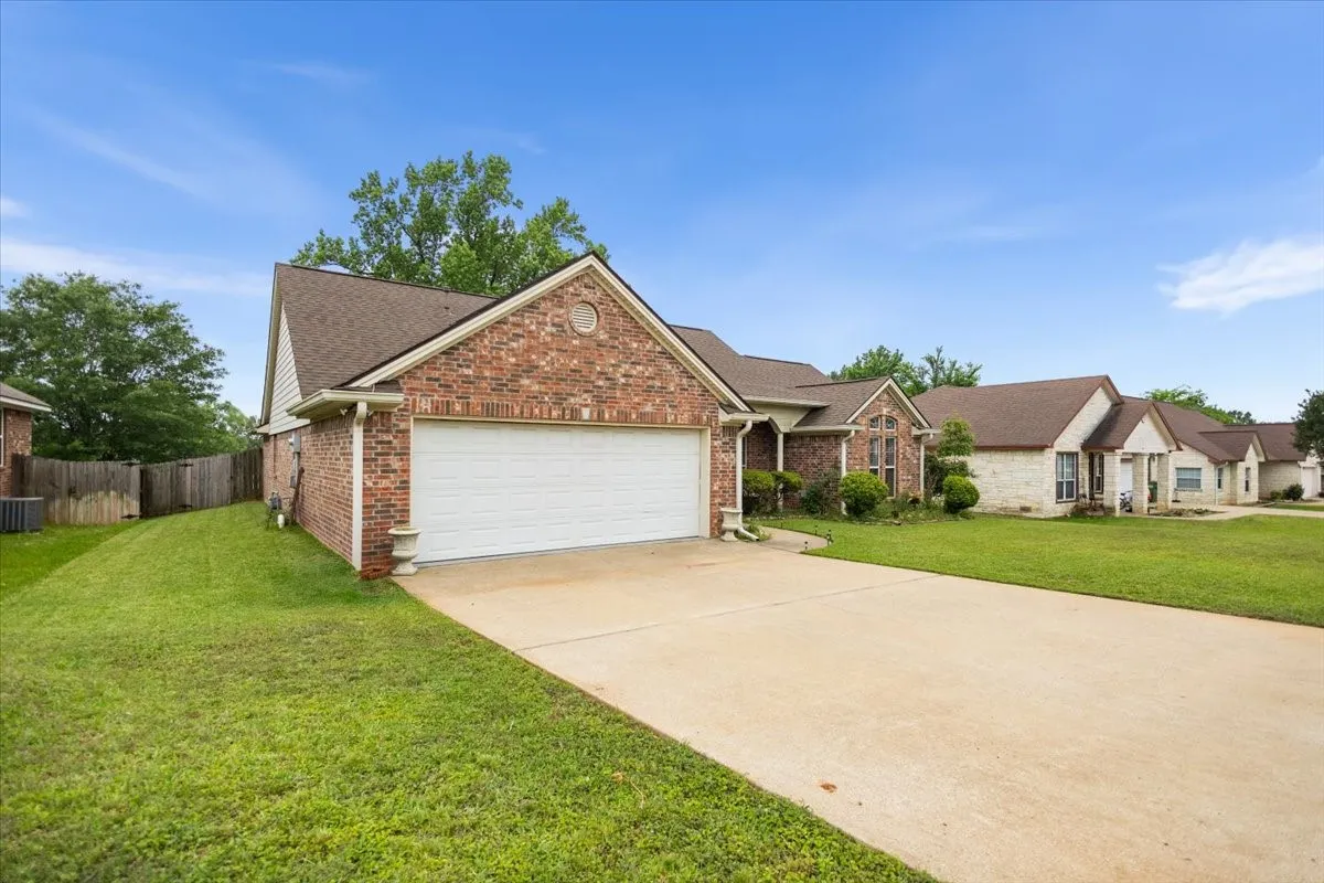 Brick facade residence featuring an attached two-car garage, concrete driveway, and front lawn