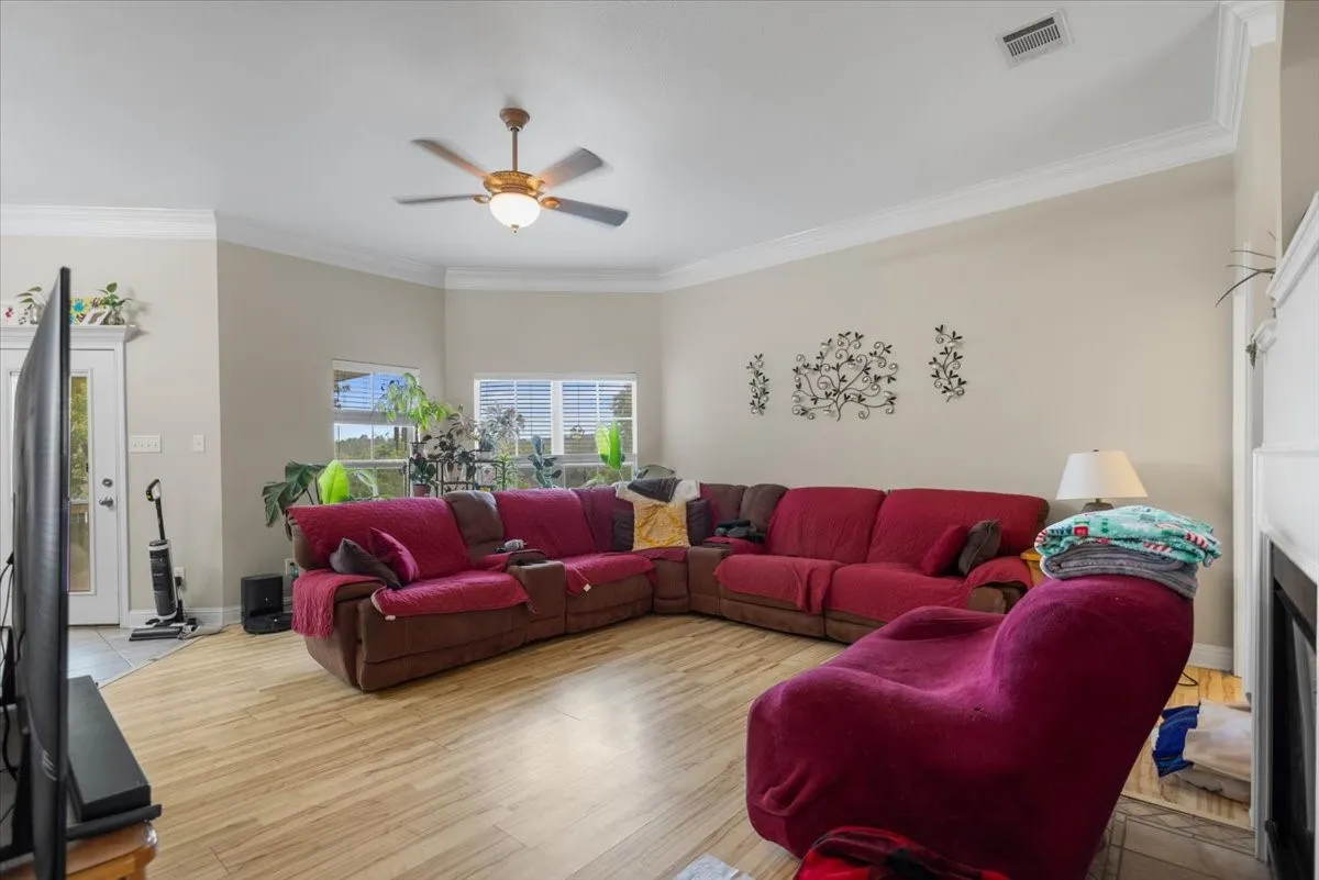 Living area featuring wood-finish flooring, a ceiling fan with integrated lighting, and multiple windows