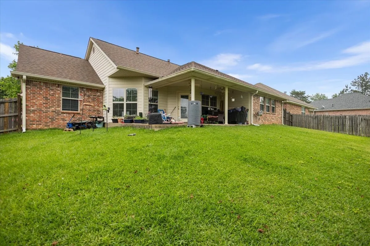 Expansive backyard featuring a covered patio, brick exterior, vinyl siding, and a wooden privacy fence