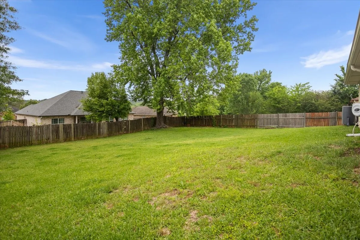Expansive backyard featuring a manicured lawn, established shade trees, and a full perimeter wood fence