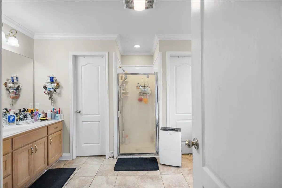 Bathroom featuring a dual vanity, glass-enclosed shower, tiled flooring, and multiple white panel doors