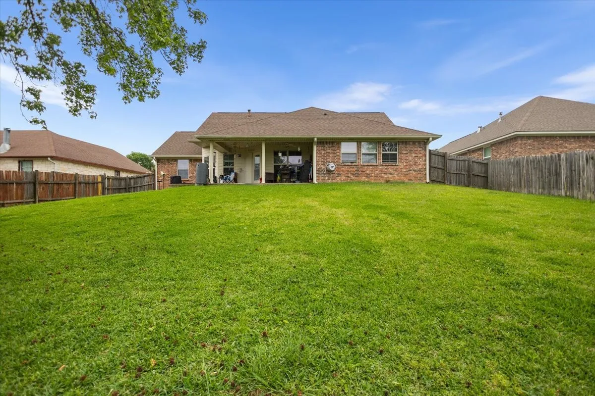 Expansive green lawn with a covered patio, brick exterior, and a wood privacy fence