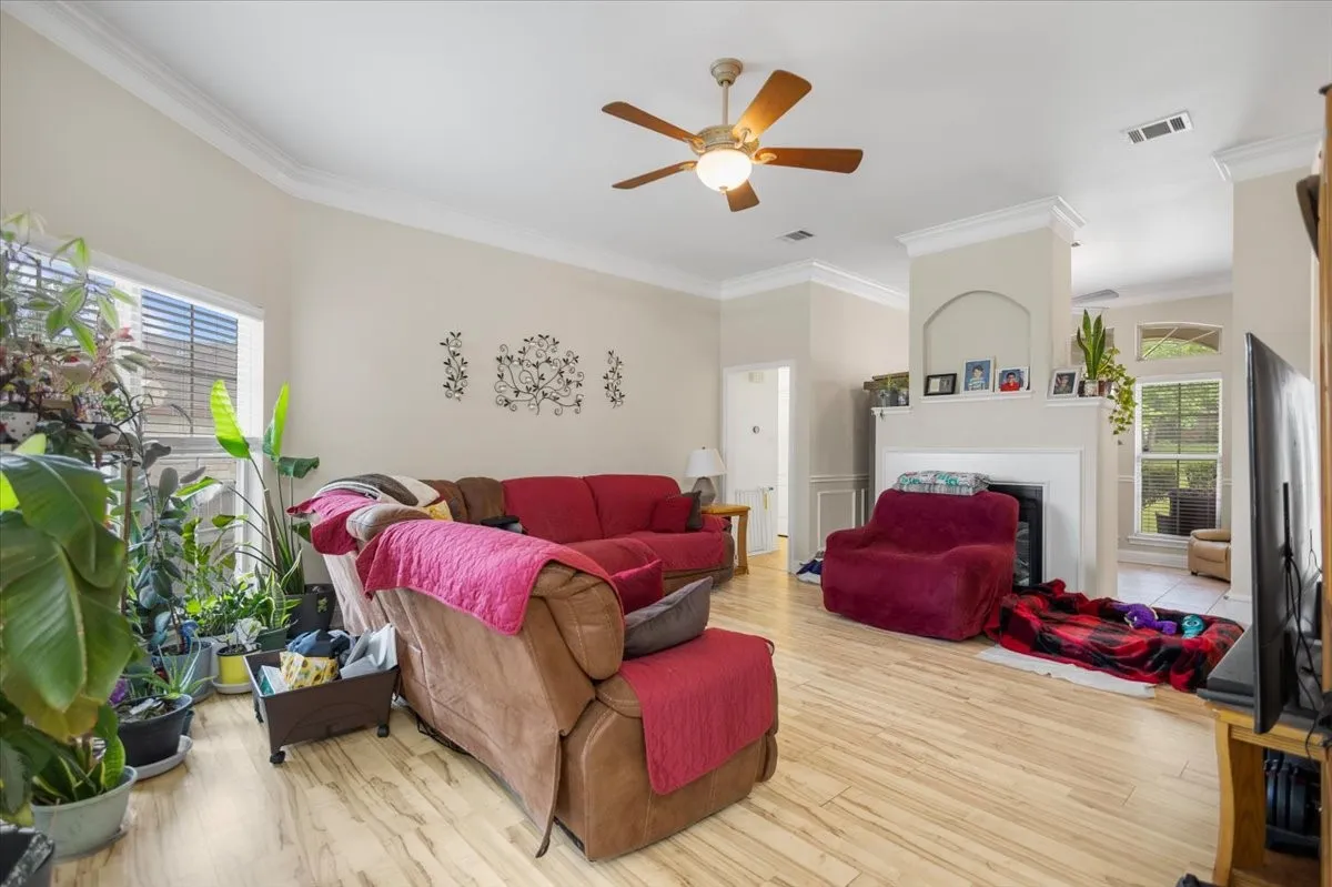 Bright living area featuring wood-finish flooring, a ceiling fan, and crown molding