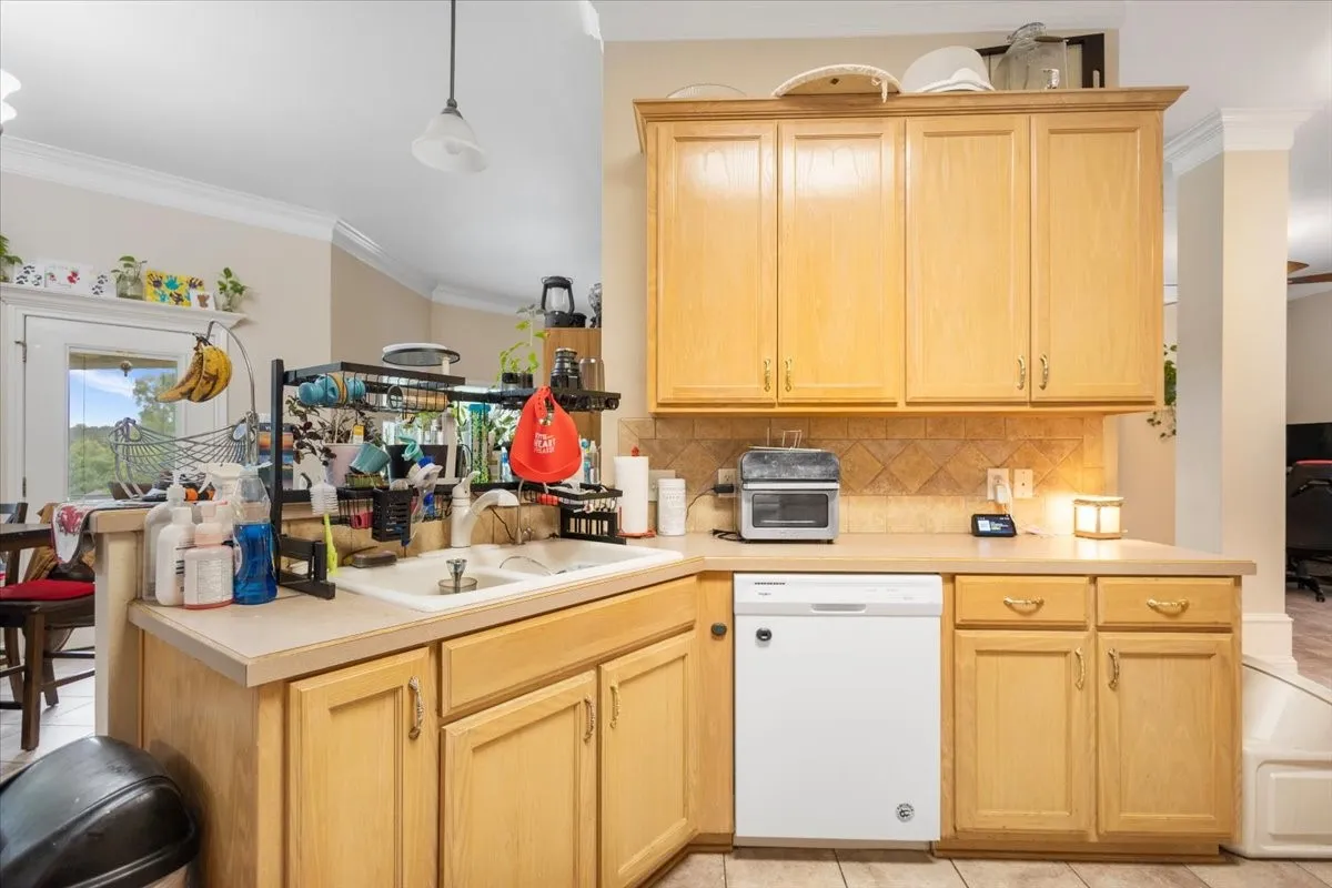 Kitchen featuring light wood cabinetry, a double basin sink, neutral countertops, and a white dishwasher