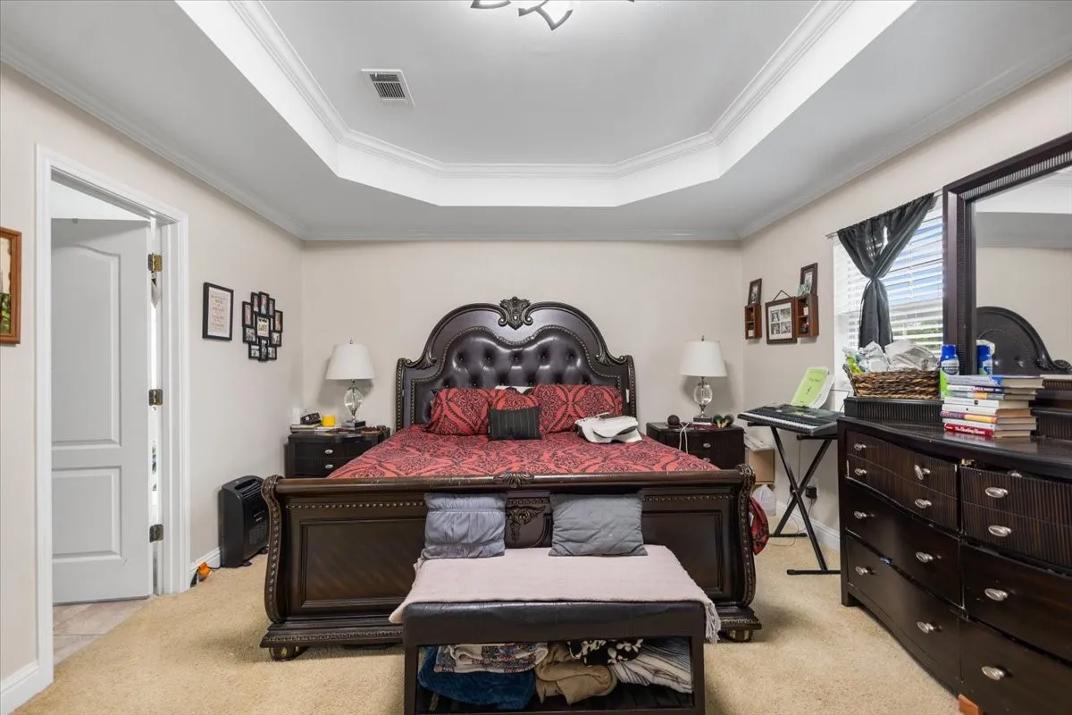 Spacious room featuring a decorative tray ceiling with crown molding, neutral wall color, and carpet flooring