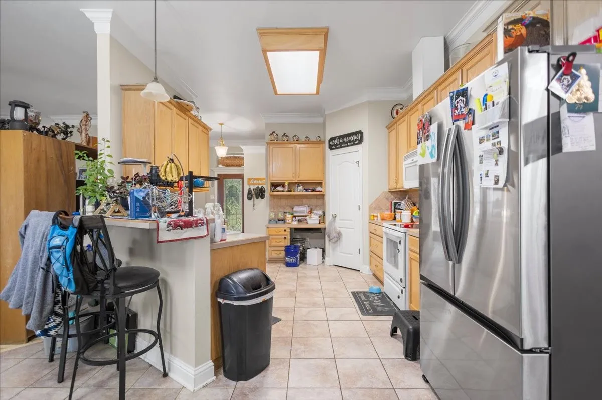 Kitchen featuring light wood cabinetry, a large stainless steel refrigerator, tile flooring, and recessed lighting