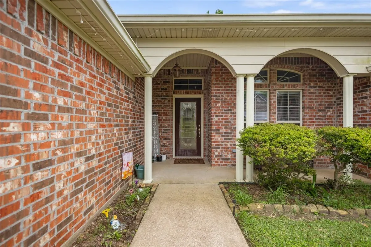Brick exterior featuring a covered entry, arched columns, a glass-panel front door, and a concrete walkway