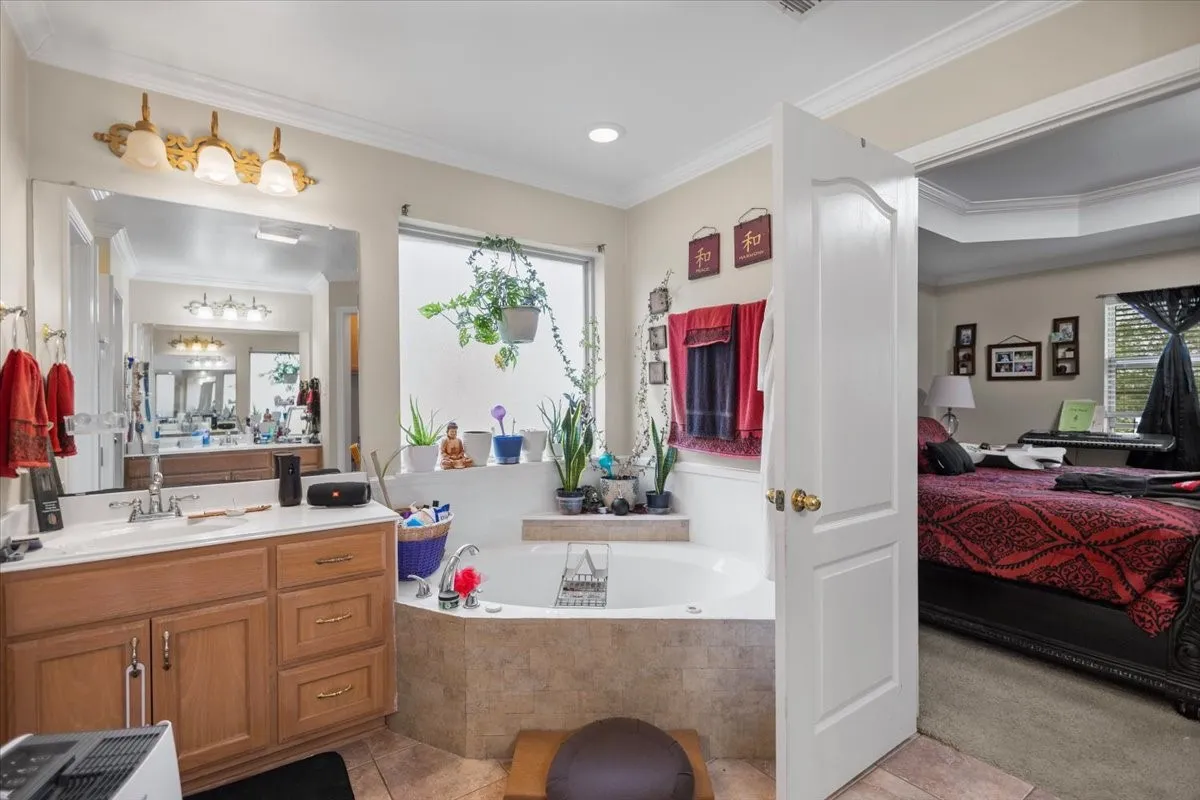 Bathroom featuring a built-in corner soaking tub with tile surround, a single vanity with wood-finish cabinetry and integrated sink, a large wall-mounted mirror, and a frosted window providing natural light