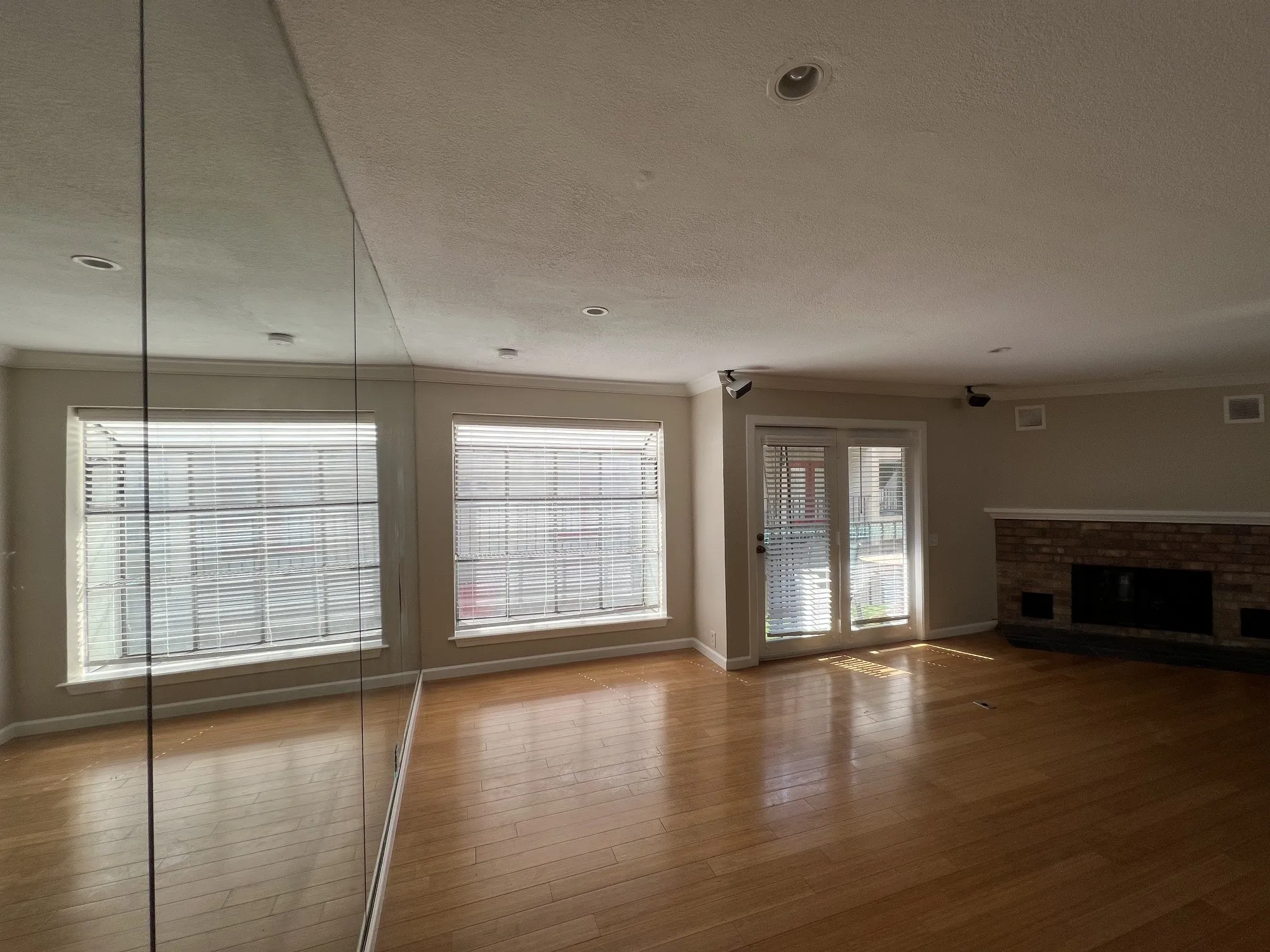 Hardwood flooring, brick-surround fireplace, dual French doors, recessed lighting, and expansive mirrored wall