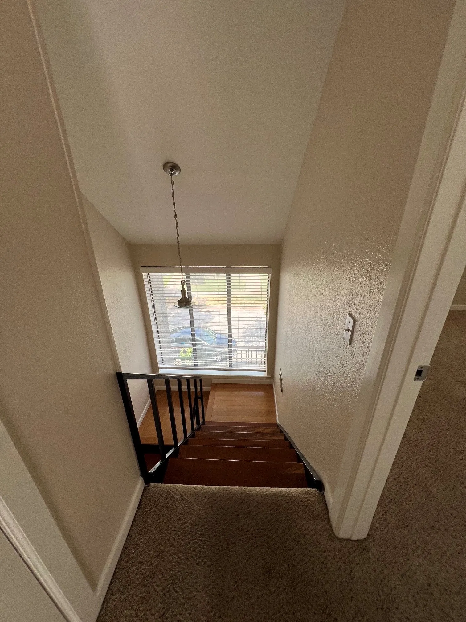 Looking down staircase featuring wood-finish treads, black metal railing, and a window with blinds
