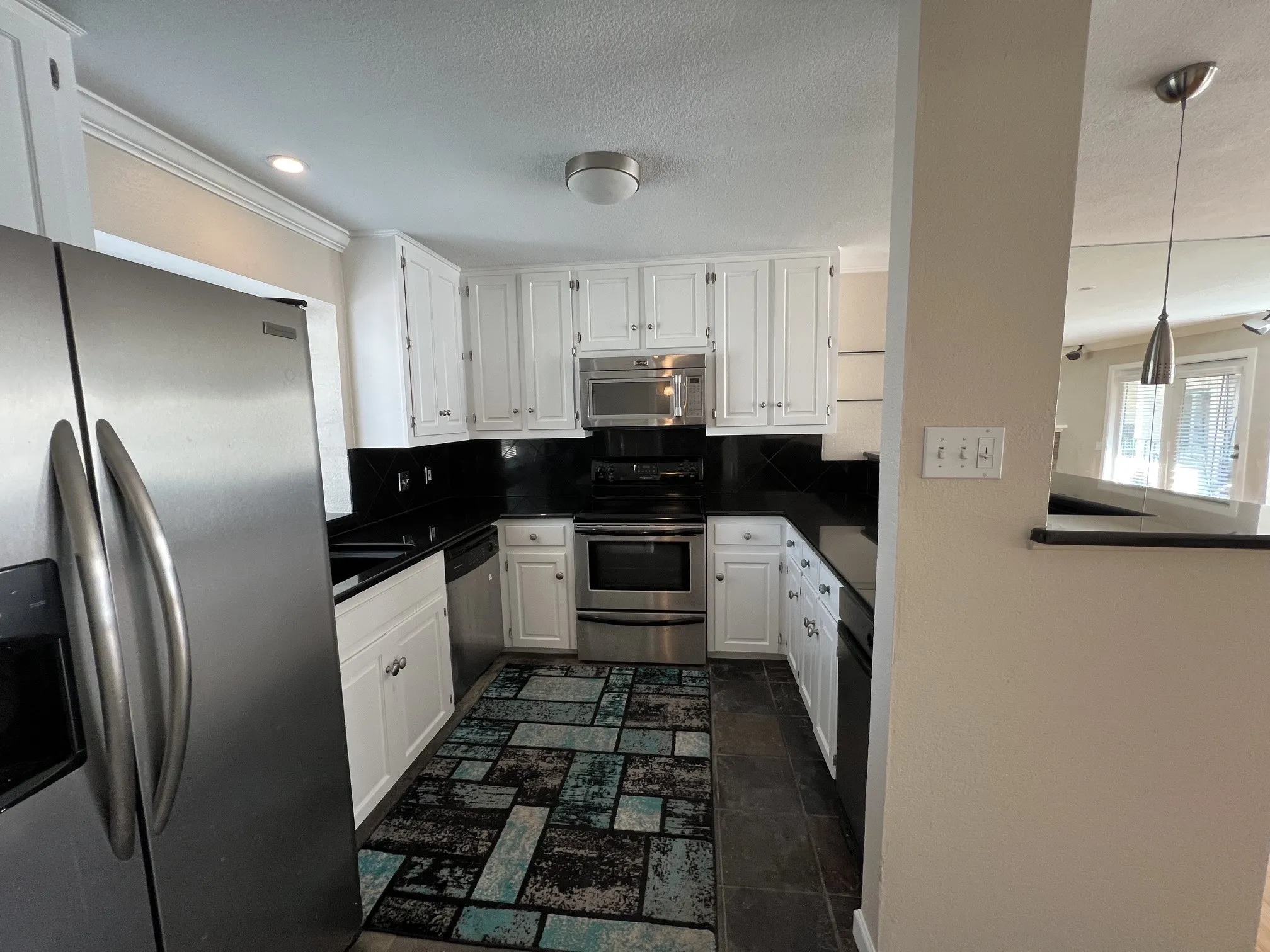 Kitchen featuring white cabinetry, black granite countertops, dark tile backsplash, stainless steel appliances and real stone floor tiles.