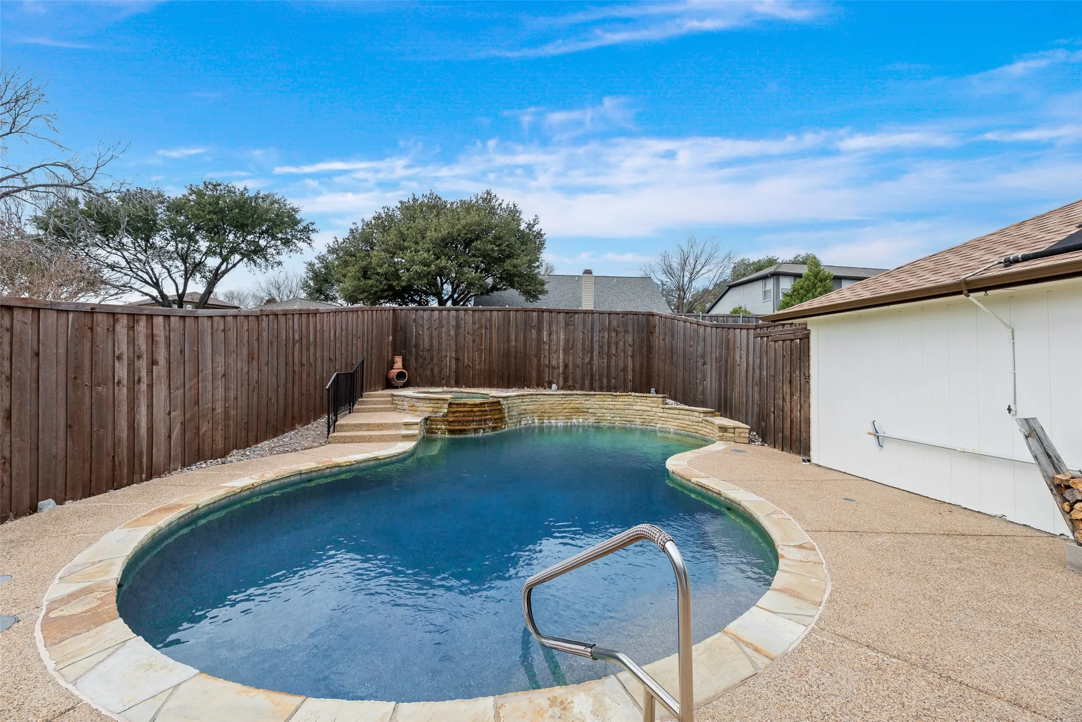 Backyard oasis featuring a freeform swimming pool with stone coping, a raised spa with a waterfall, and stone steps