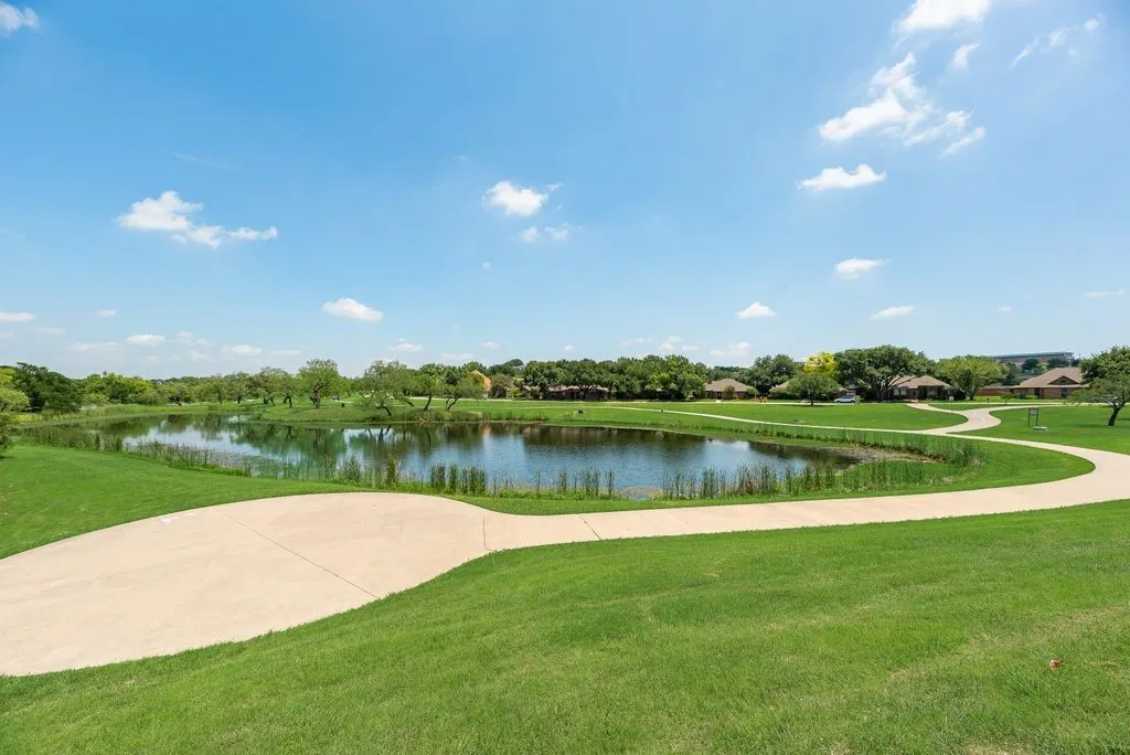 Expansive green space featuring a curved concrete pathway and a tranquil pond with natural vegetation