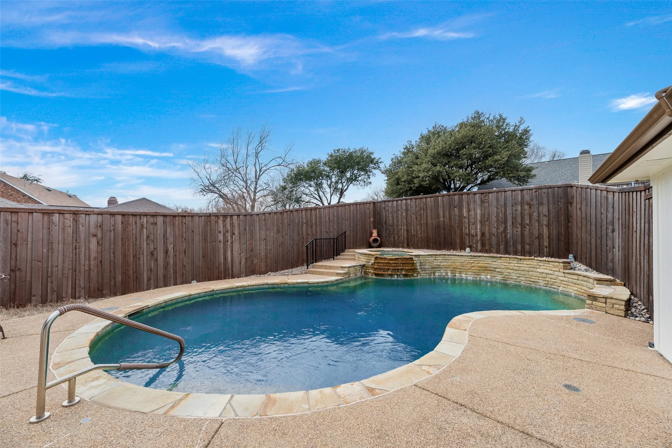 Custom-shaped swimming pool featuring a waterfall, stone-clad spa, and a flagstone coping