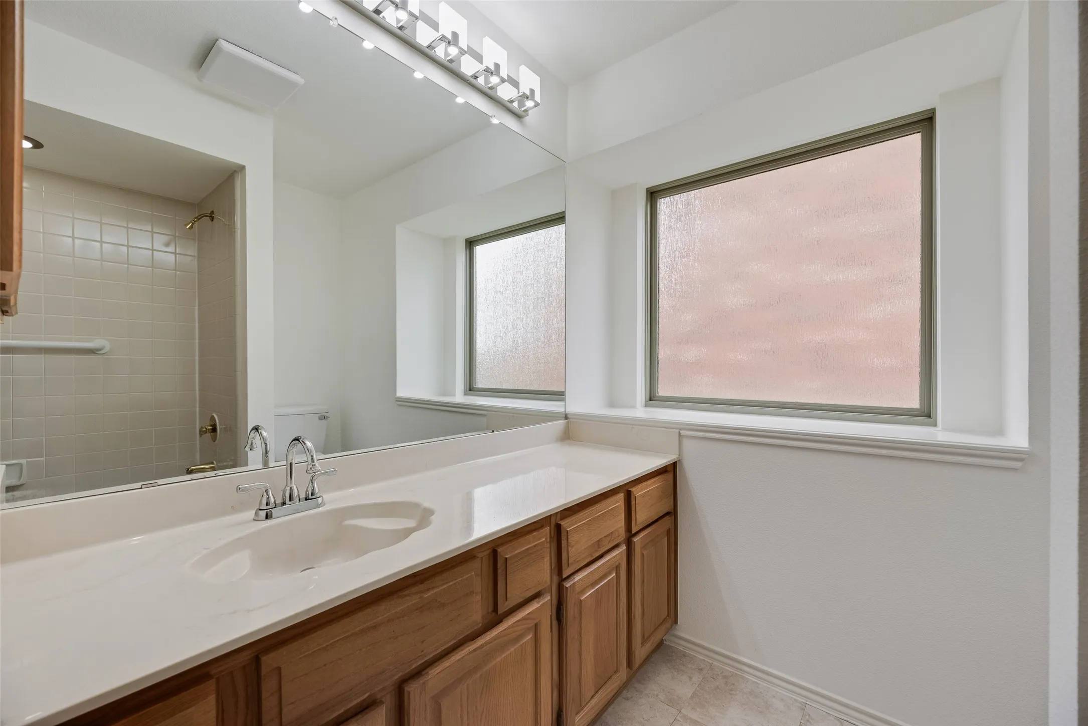 Bathroom vanity with light wood-finish cabinetry, a single integrated sink, and chrome faucet