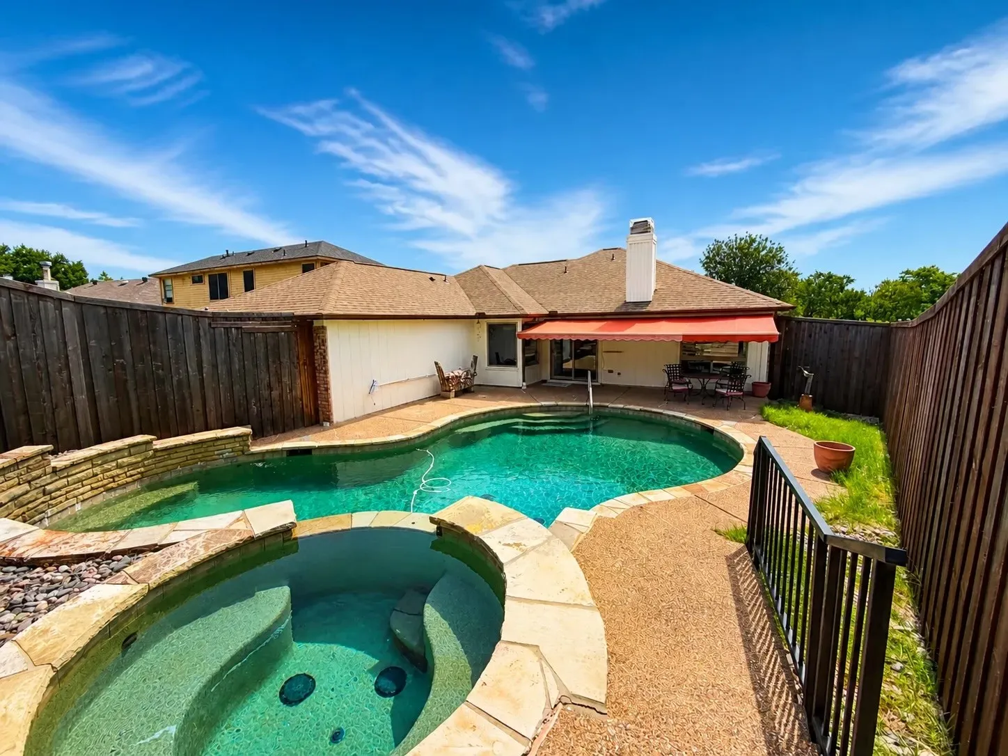 Custom-shaped swimming pool with an integrated spa, stone coping, and a textured concrete deck