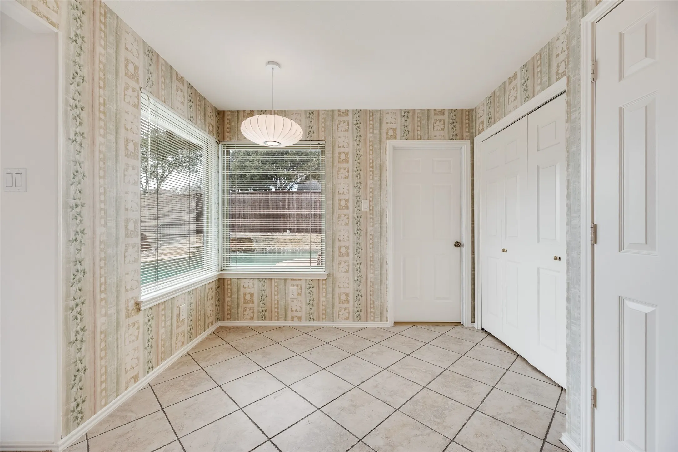 Room featuring ceramic tile flooring, patterned wallpaper, and a corner window arrangement