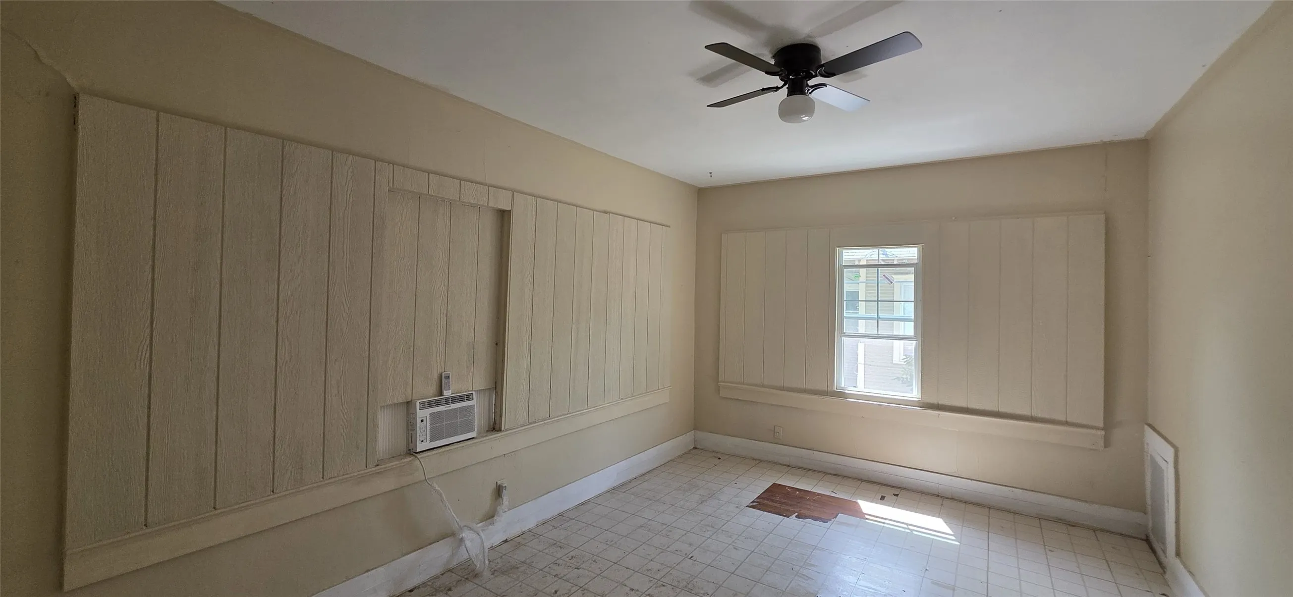 Interior room featuring a ceiling fan, light-colored wall paneling, a window, and tiled flooring