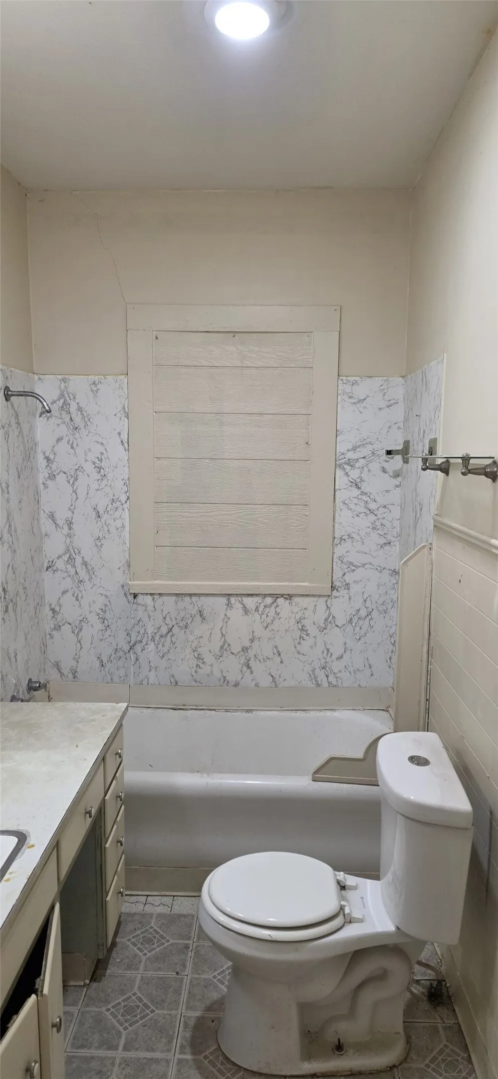 Bathroom featuring a bathtub, toilet, vanity with storage, patterned floor tiling, and wall-mounted light fixture