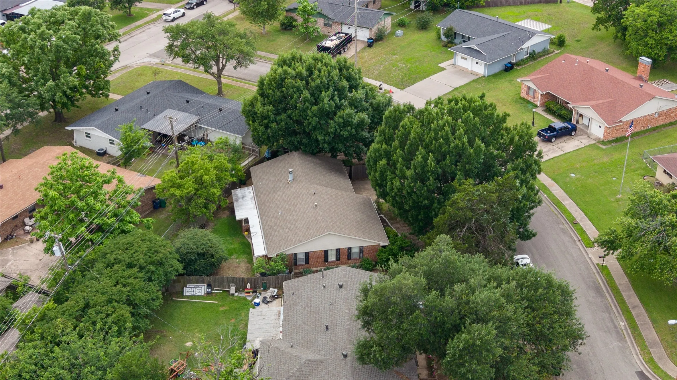 Residential property with a brown shingle roof, brick exterior, and mature trees