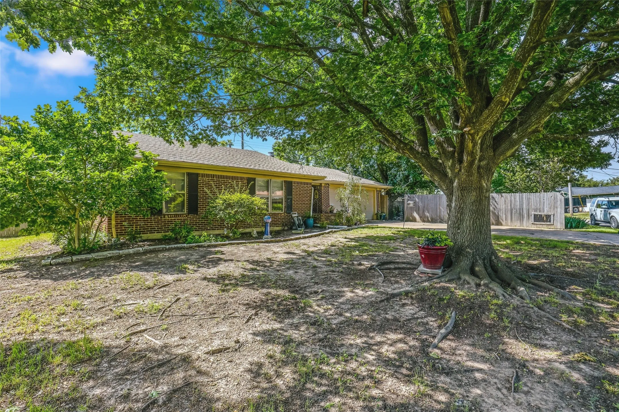 Expansive front yard featuring a large mature tree, brick exterior, dark window shutters, and established landscaping