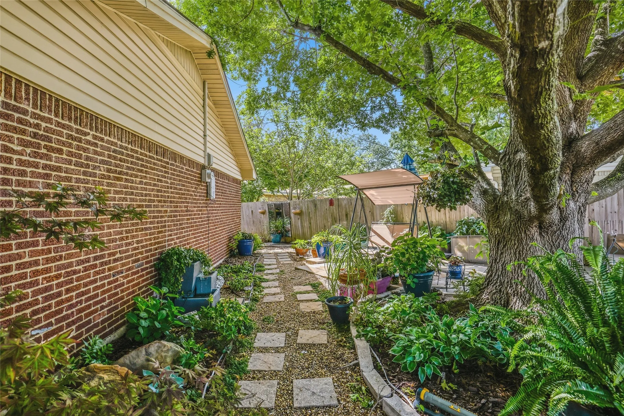 Side yard featuring a stone paver pathway, mature tree, brick exterior, and wood siding