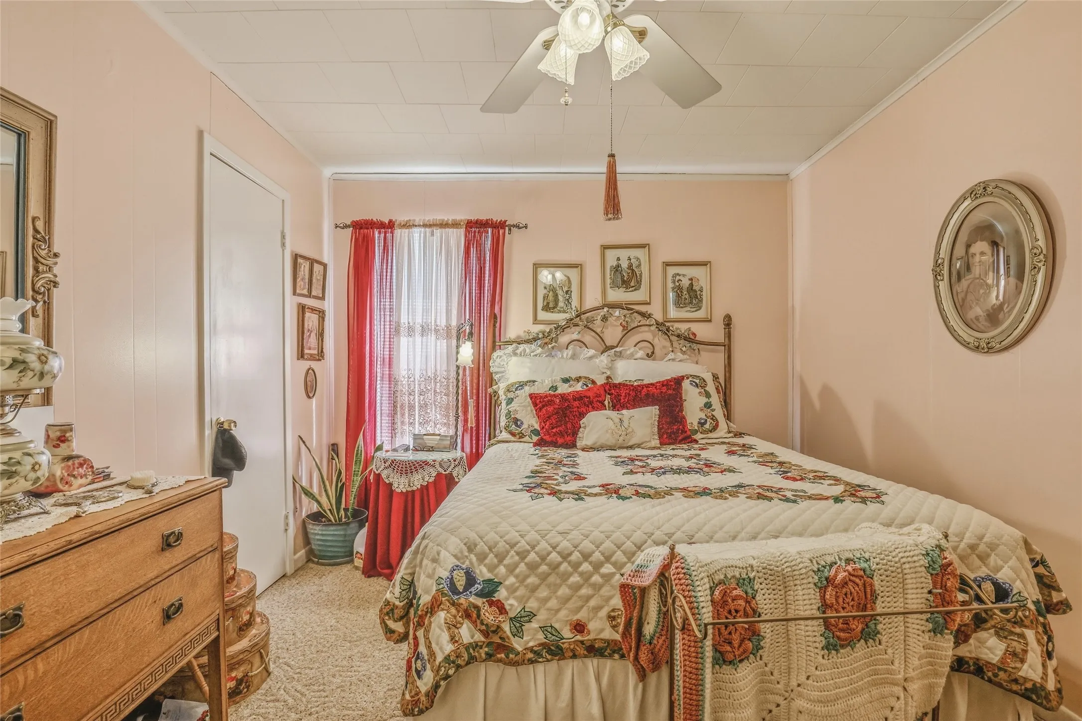 Bedroom featuring a ceiling fan with integrated lighting, wall-to-wall carpeting, and a window with sheer and red drapery