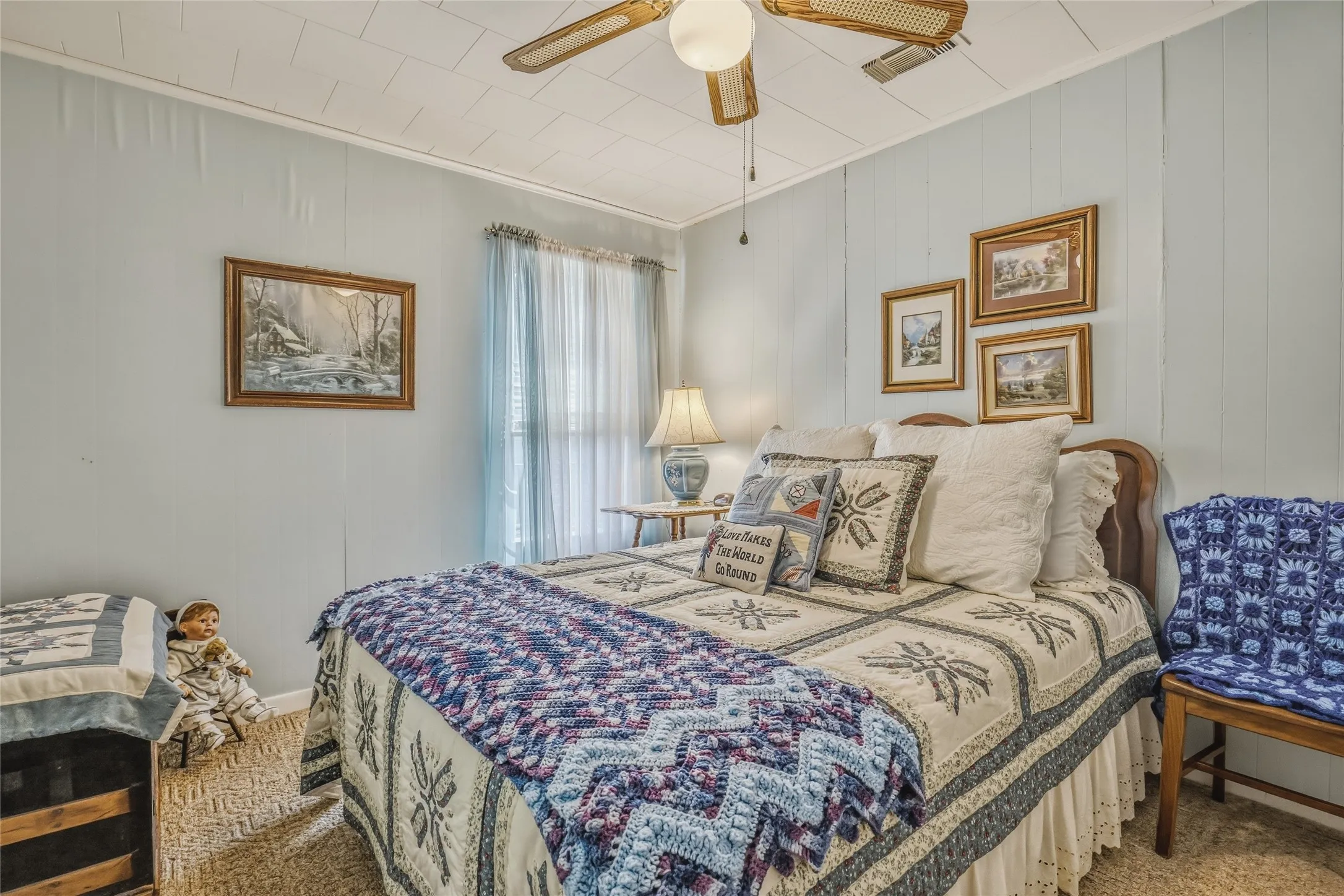 Room featuring light blue vertical paneling, a ceiling fan with woven blades, and a window with sheer drapes