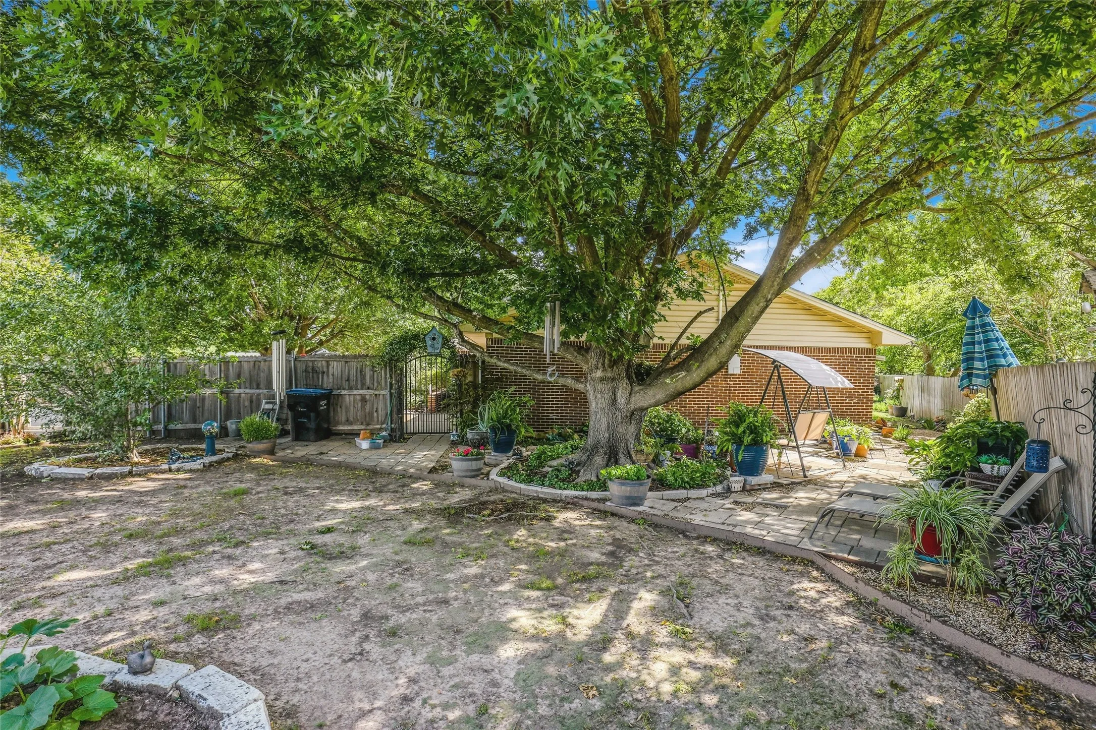 Expansive backyard featuring a mature shade tree, a stone patio area, and a brick exterior building
