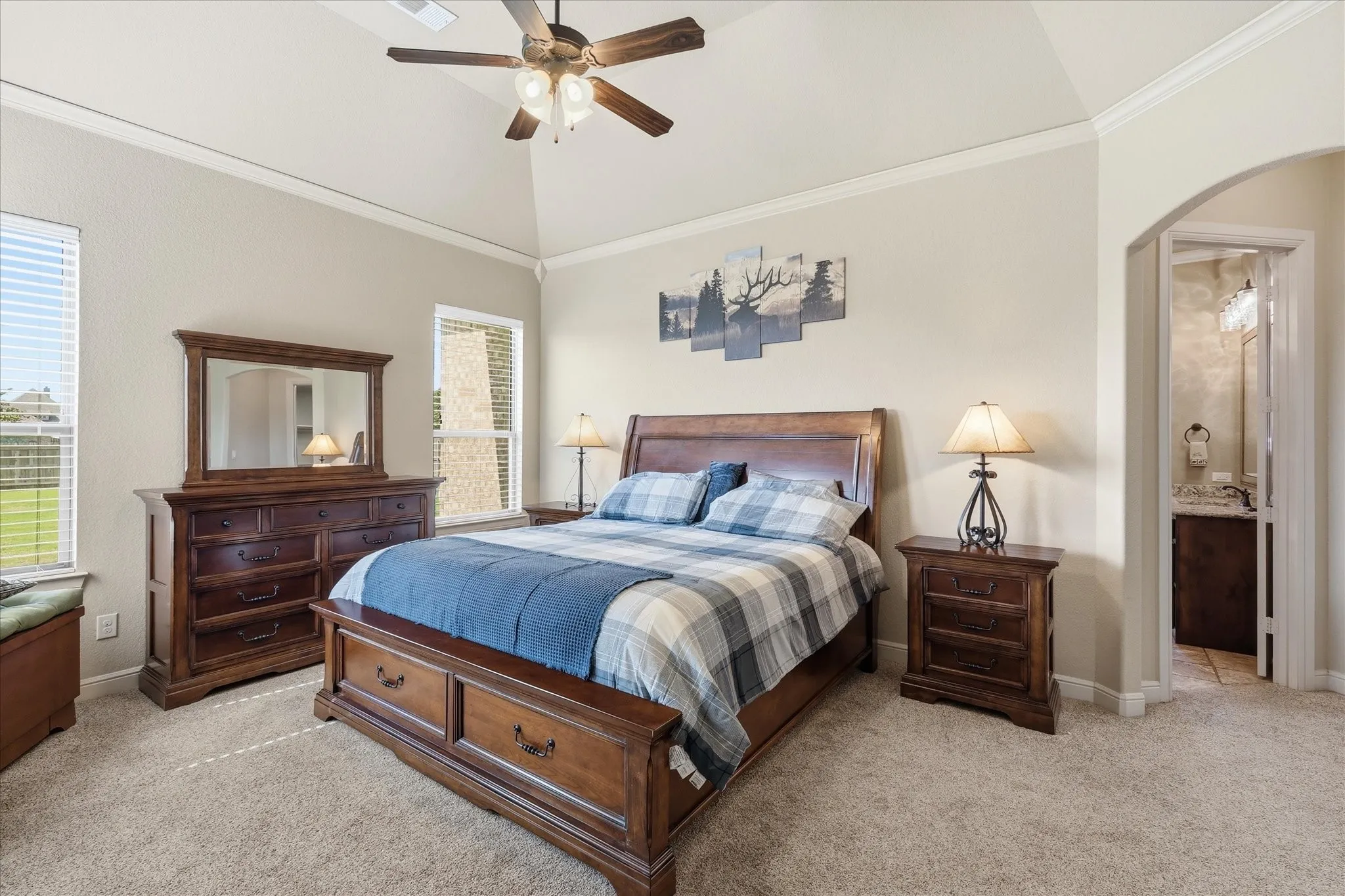 Vaulted ceiling with crown molding, carpet flooring, windows with blinds, and an arched doorway