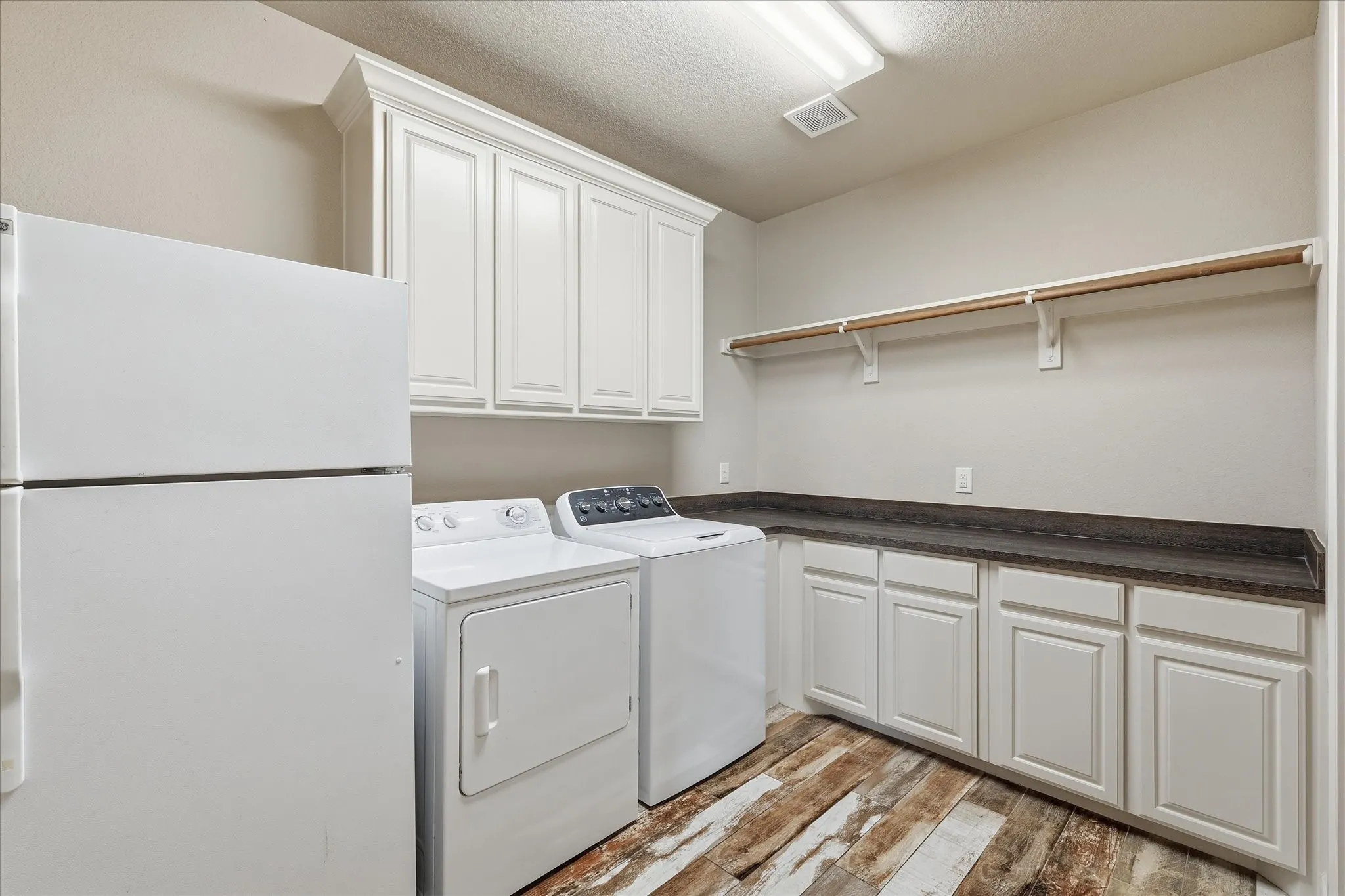 Laundry room featuring wood-finish flooring, white cabinetry, dark countertops, and a clothing rod with shelving
