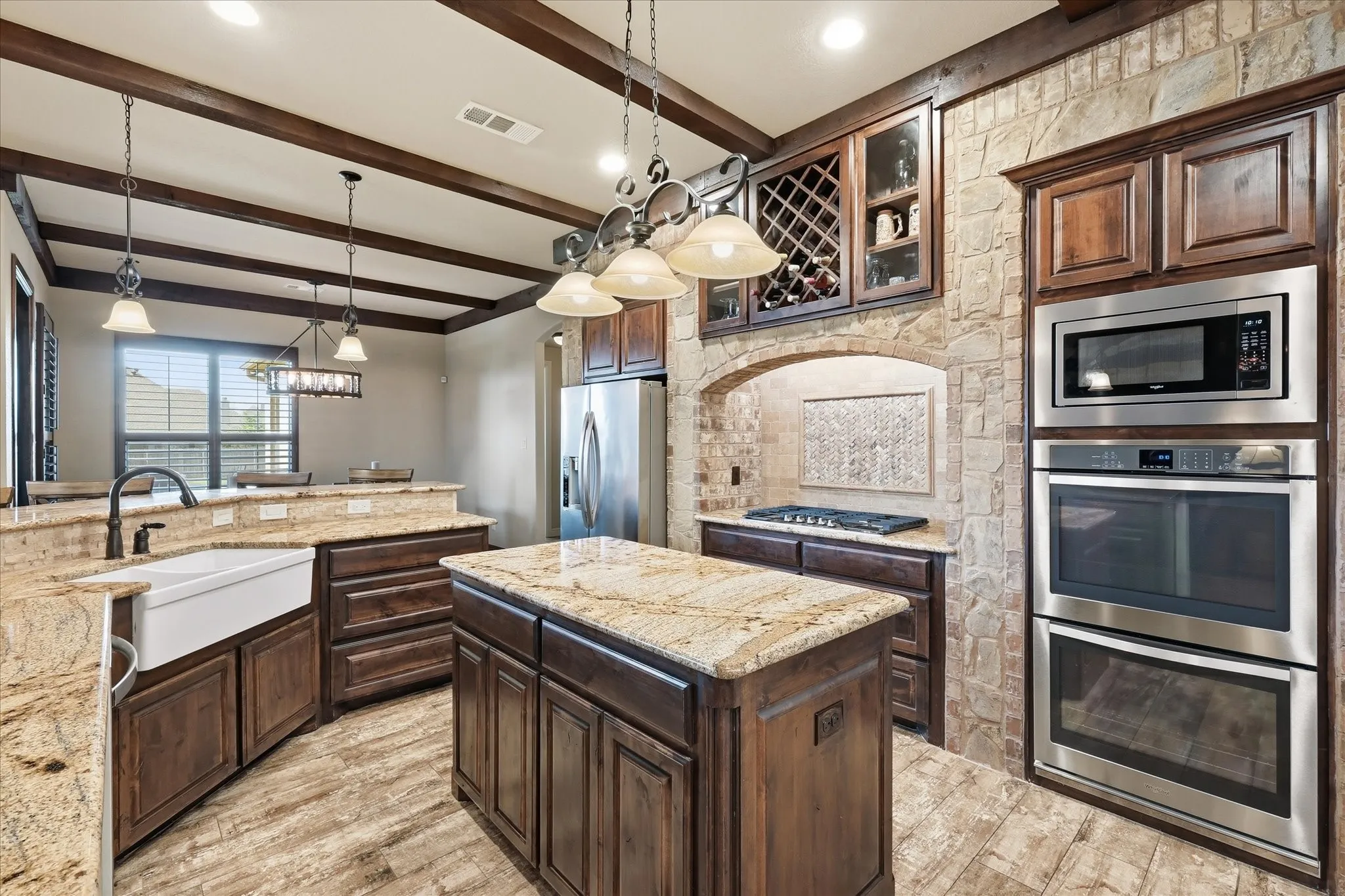Kitchen featuring exposed ceiling beams, rich wood cabinetry, granite countertops, a farmhouse sink, and stainless steel built-in appliances