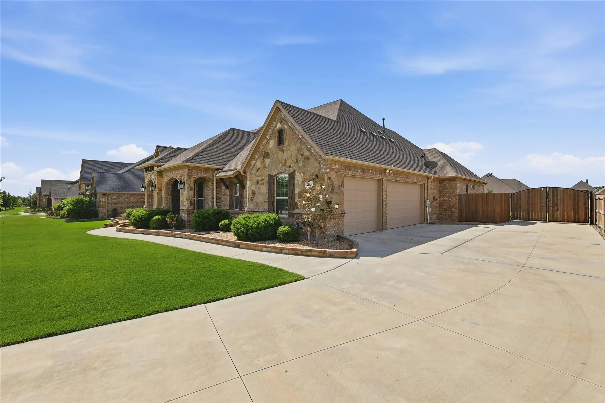 Stone facade architecture featuring a three-car garage, concrete driveway, and established landscaping