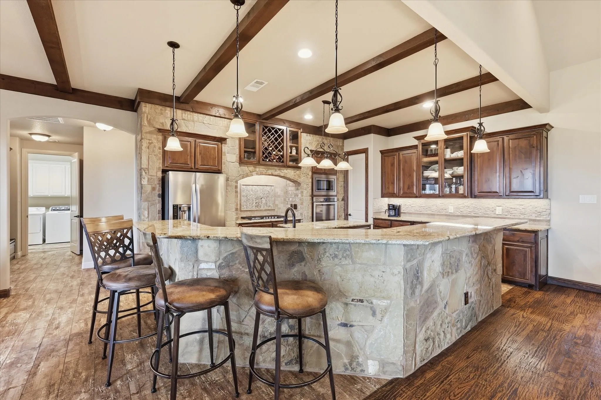 Stone-faced kitchen island with a granite countertop, complemented by dark wood-finish cabinetry, stainless steel appliances, and wood-finish flooring