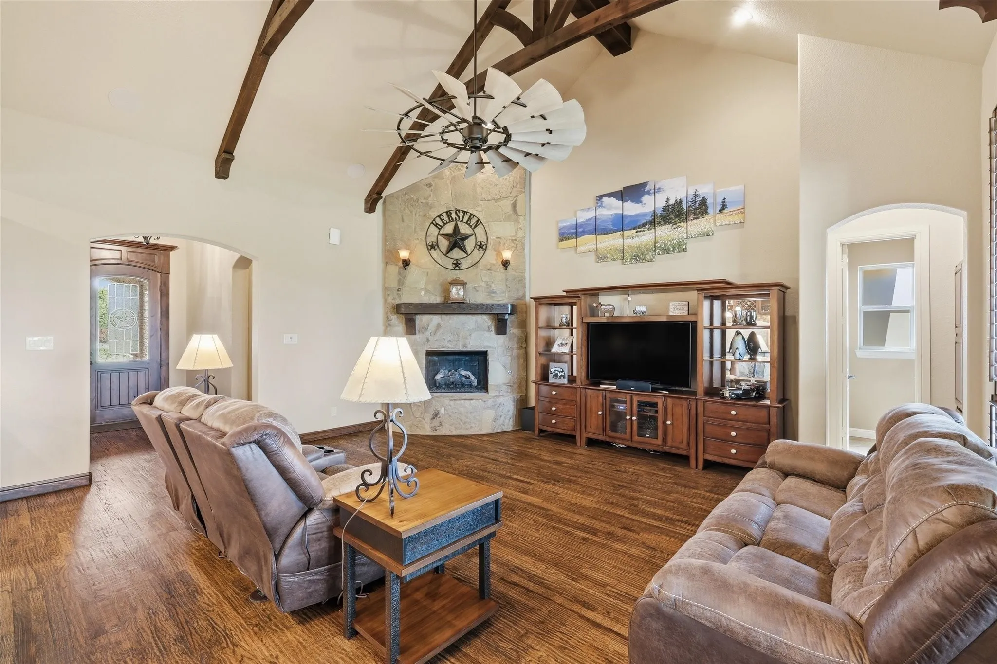 Vaulted ceiling with exposed wood beams, wood-finish flooring, stone-clad fireplace, and arched doorways