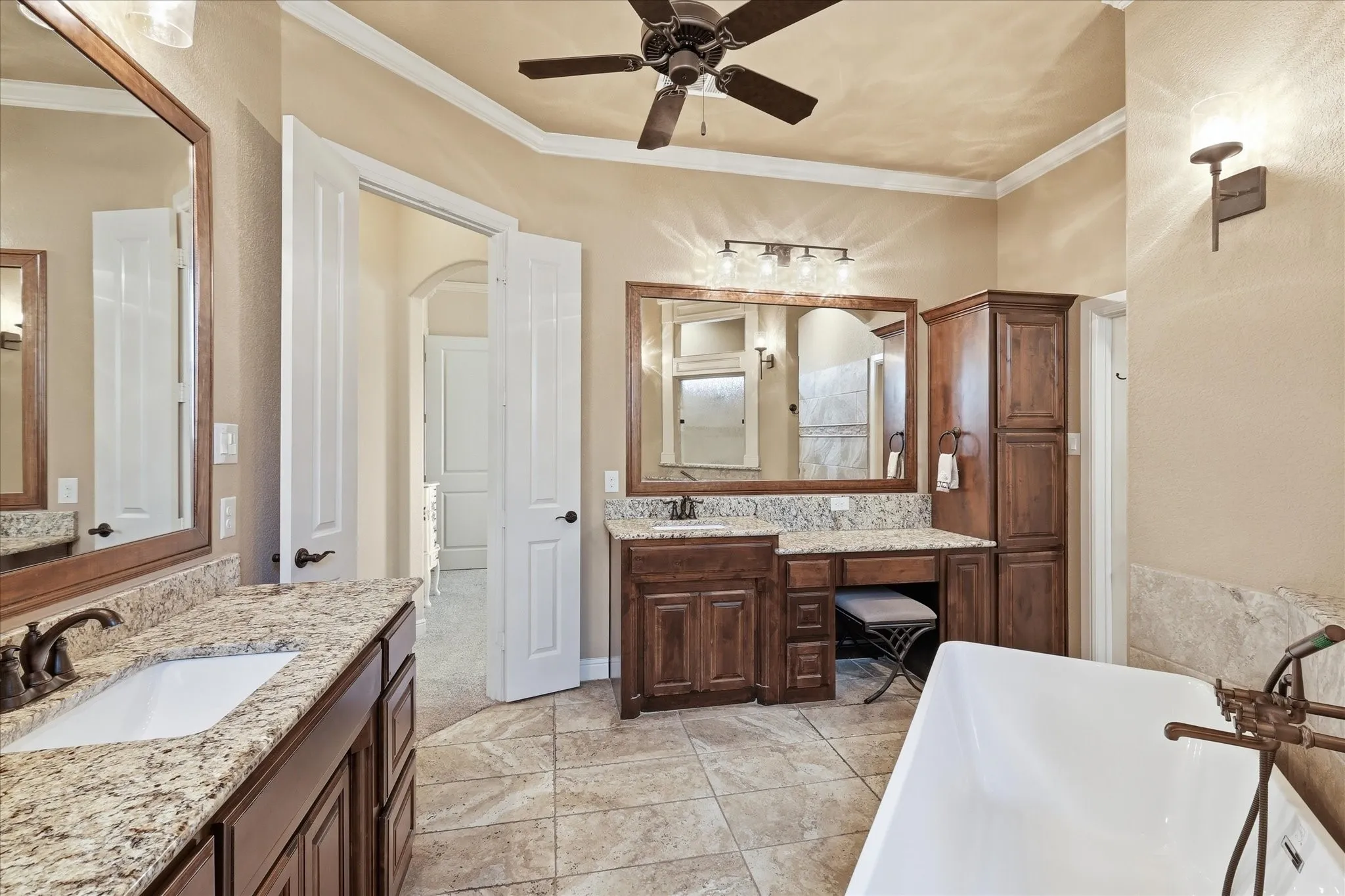 Bathroom featuring a freestanding tub, dual vanity with granite countertops, wood-finish cabinetry, and a ceiling fan