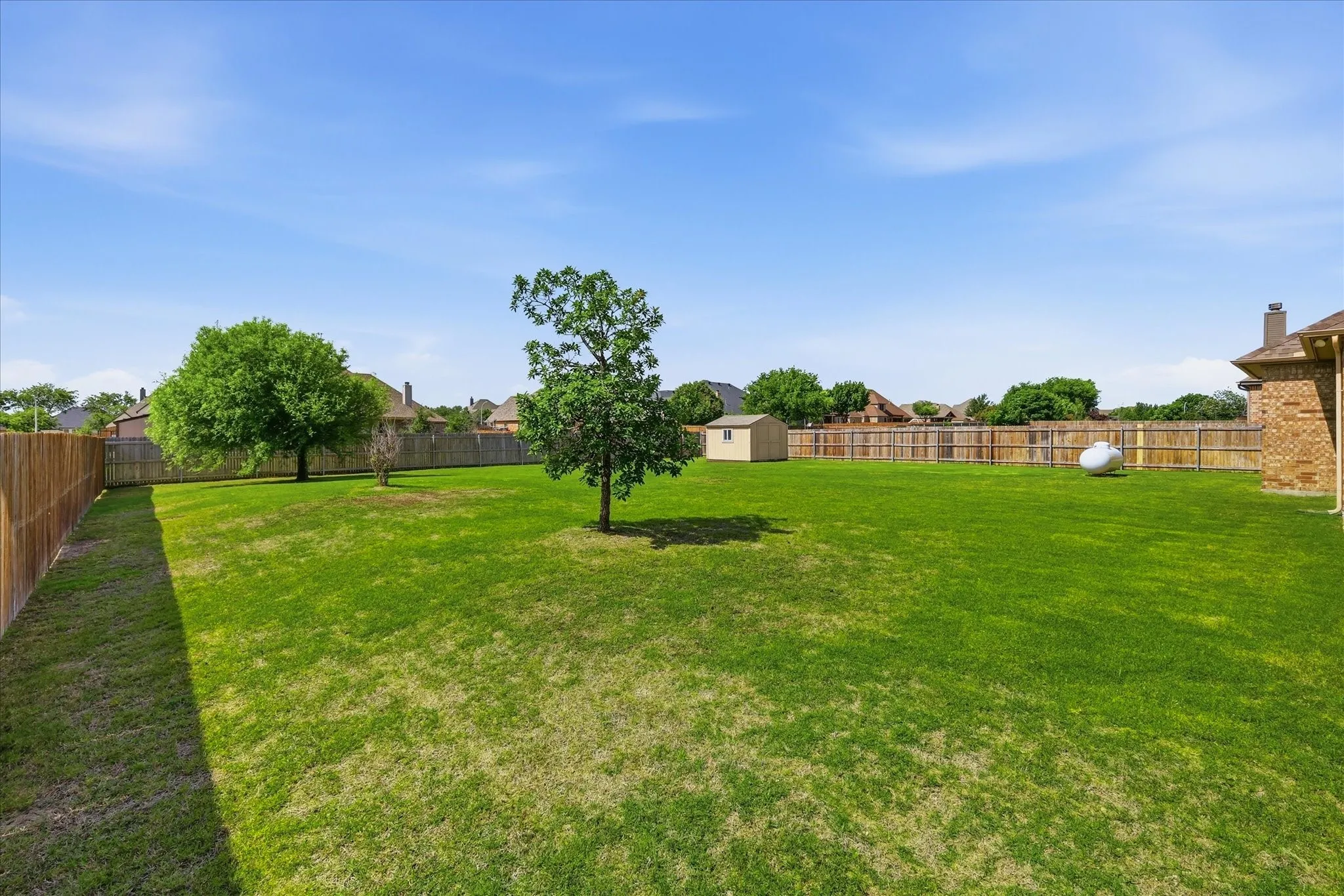 Expansive backyard with a manicured lawn, established trees, and perimeter wood fencing